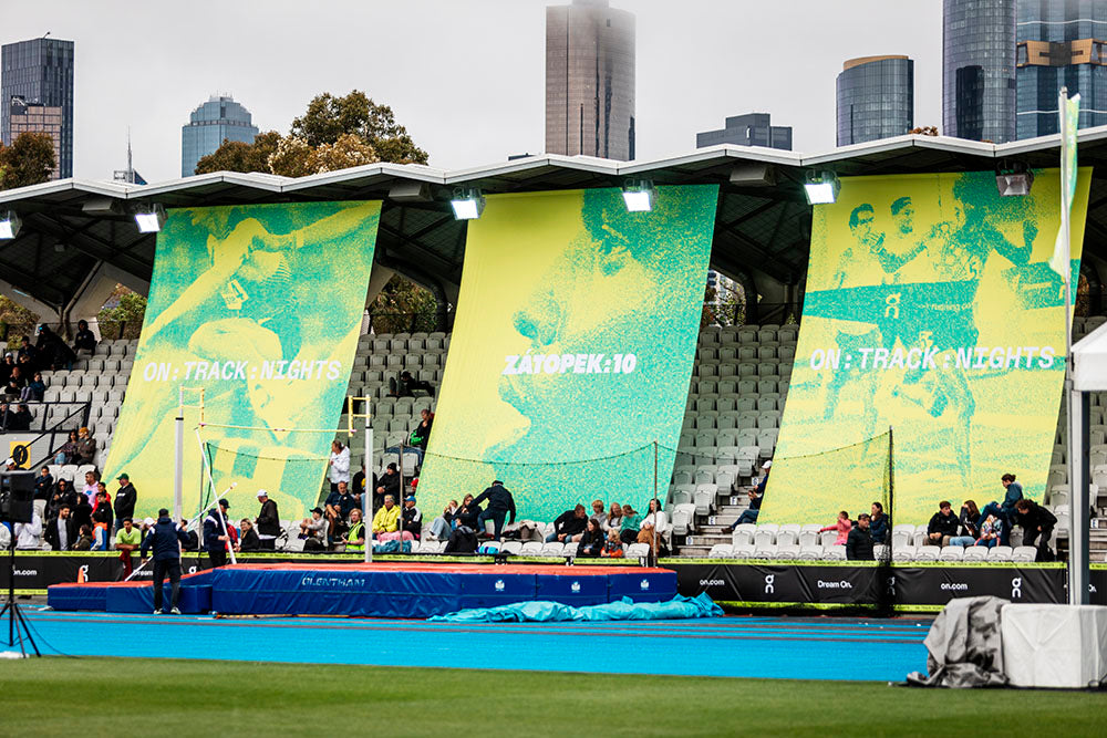Stadium with large green banners featuring athletes and text, with city skyline in the background.