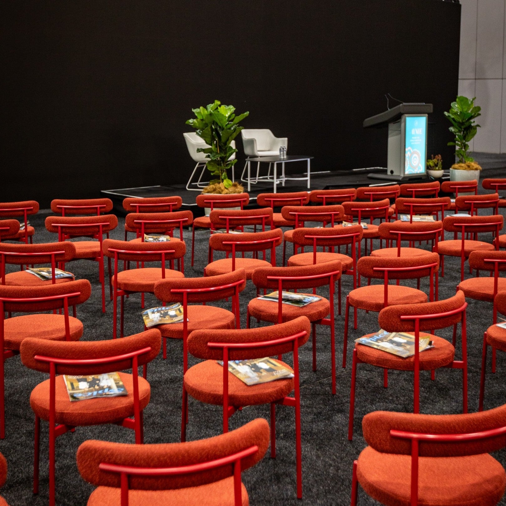 Conference room with red Margot chairs and a stage setup.