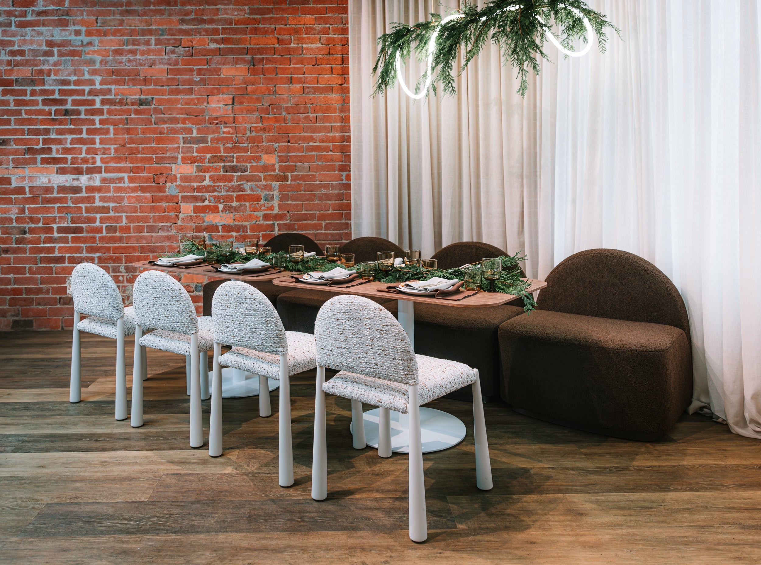 Dining area with a brick wall, white Pearl chairs, and a Harper brown sofa.