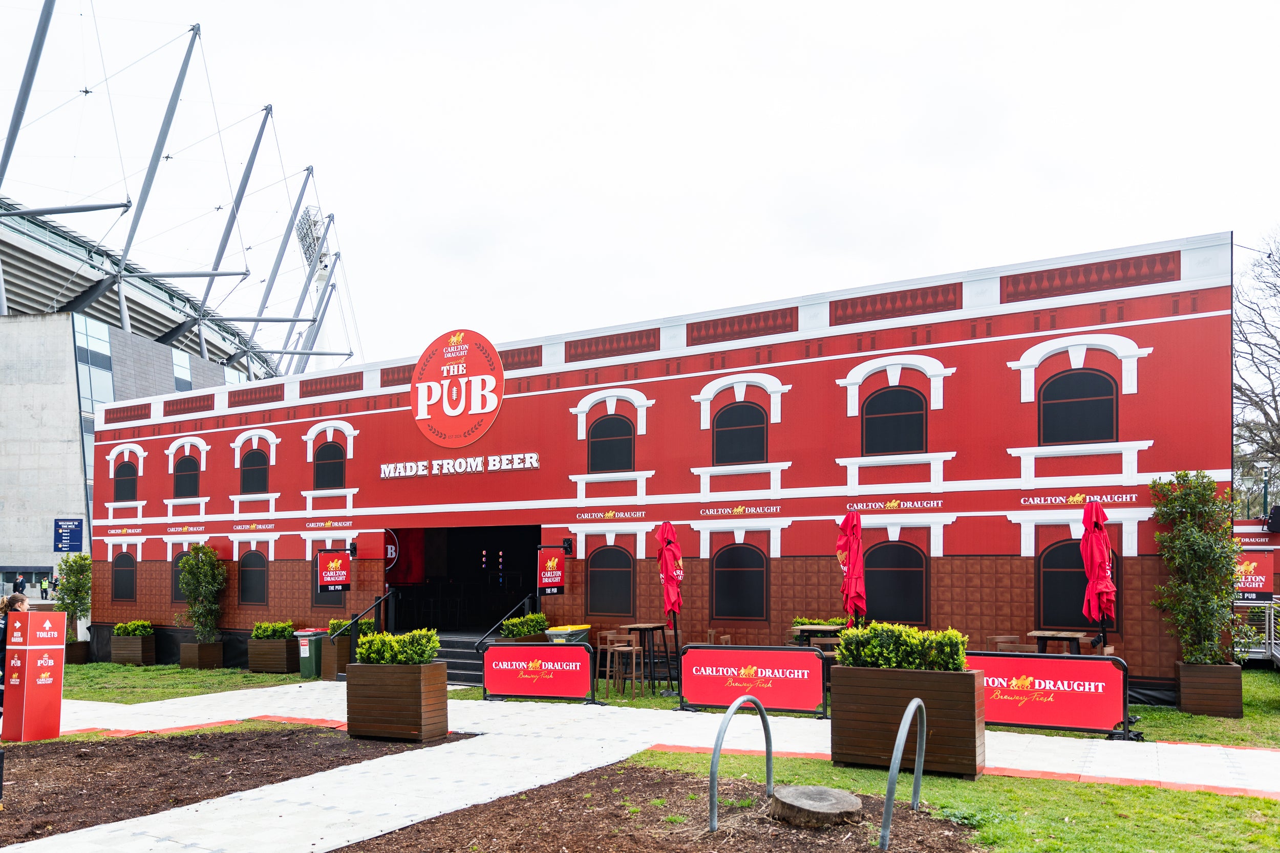 Red brick Marquee with 'The Pub' sign, outdoor seating area, and greenery.