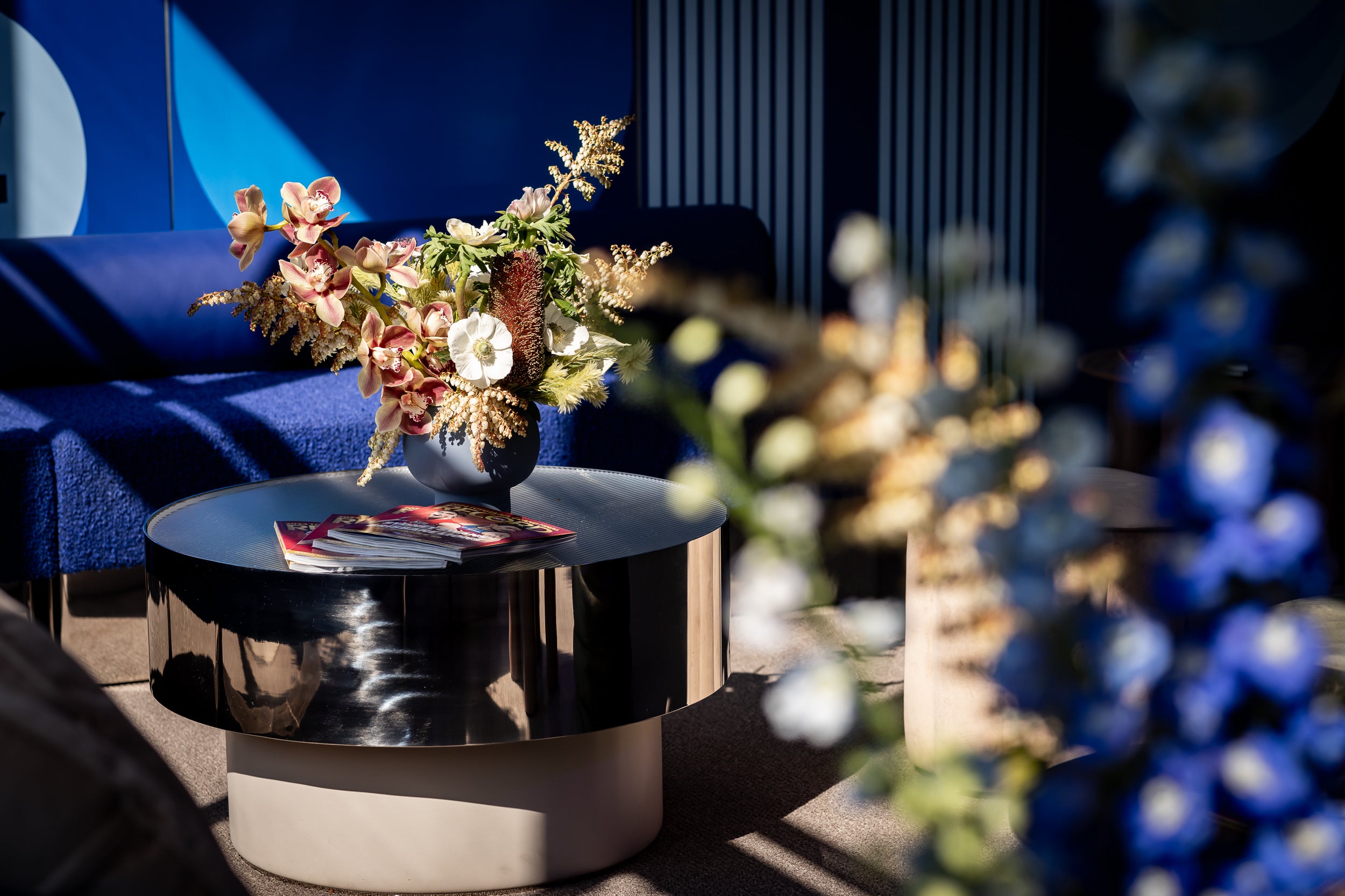 Sitting area with a blue sofa, round black coffee table, and floral arrangement at a major event
