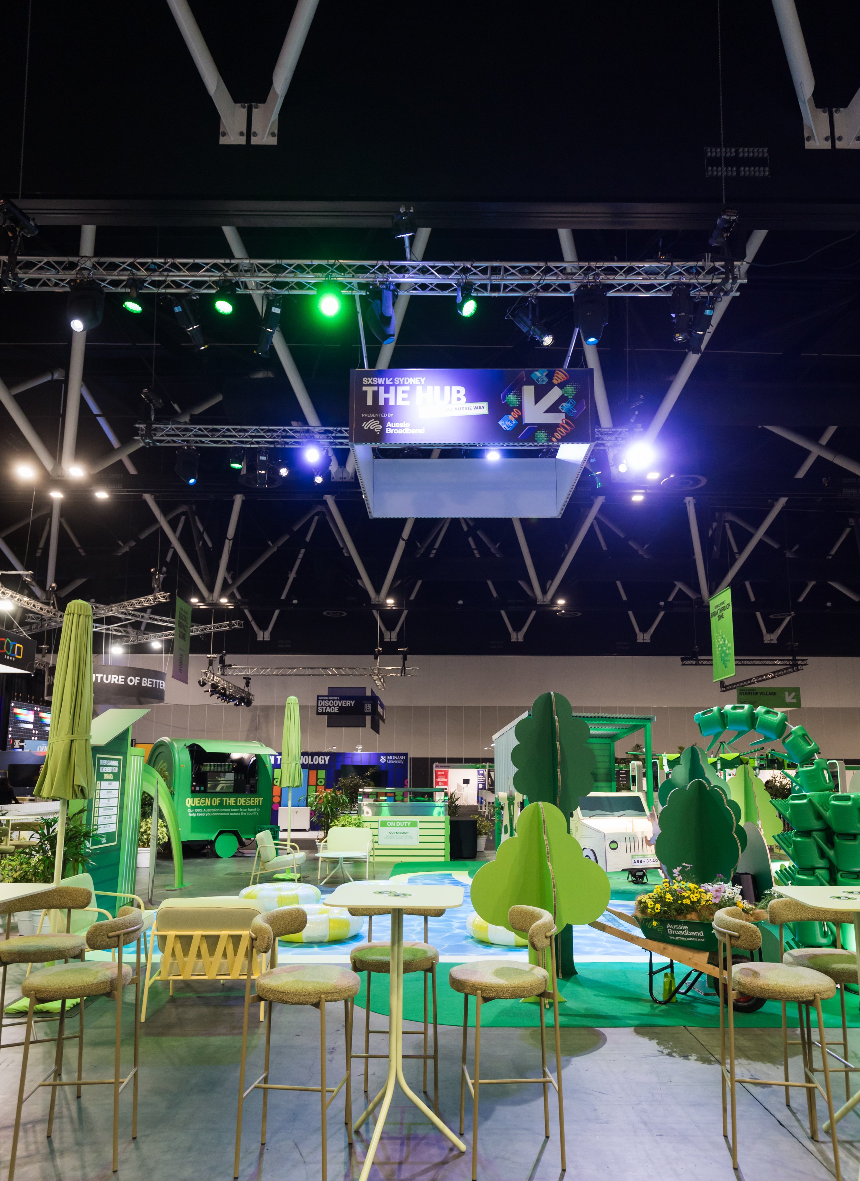 Exhibition hall with green and white setup, including tables and chairs.