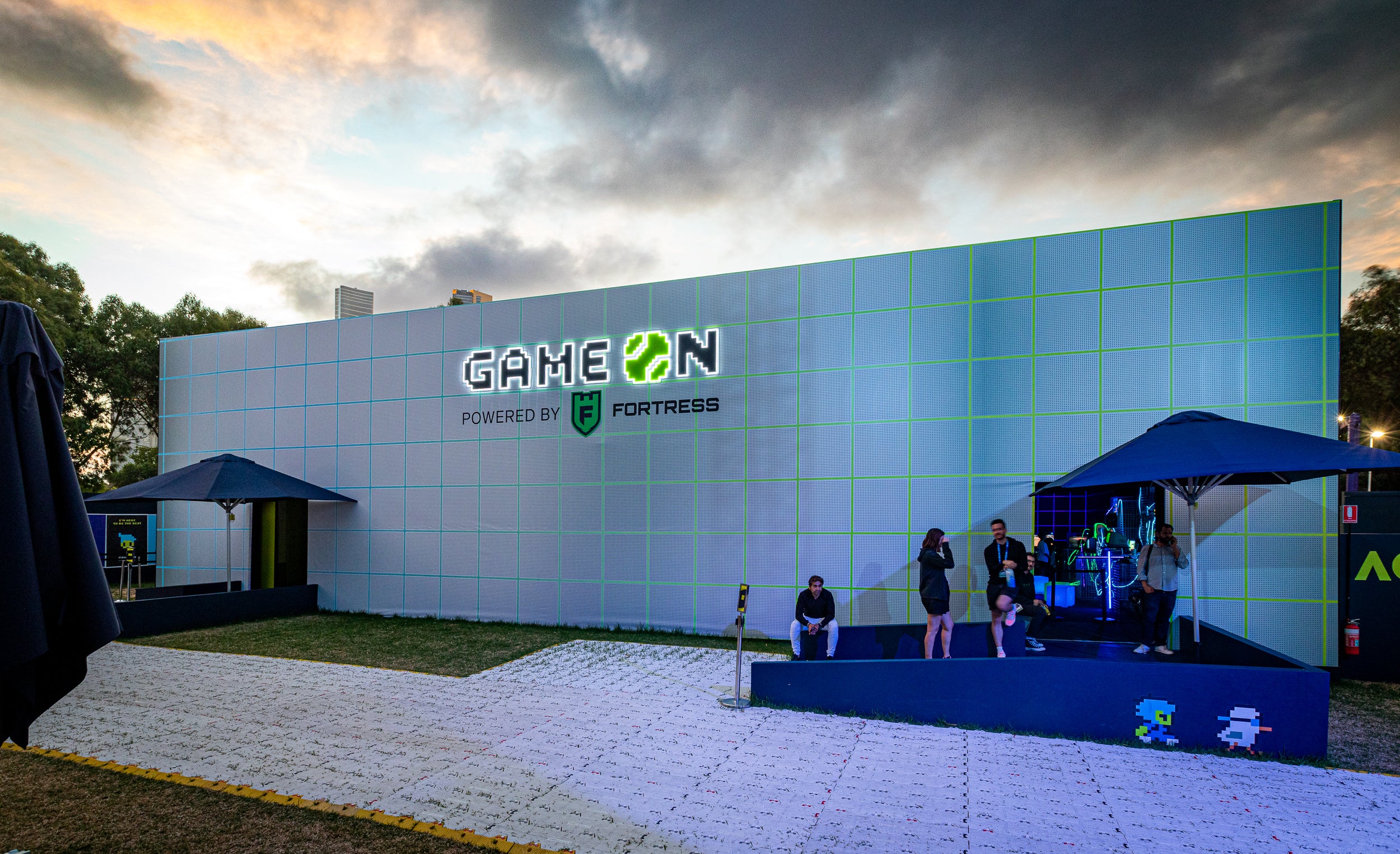 Outdoor event with 'Game ON' branded backdrop and people gathered around at Australian Open