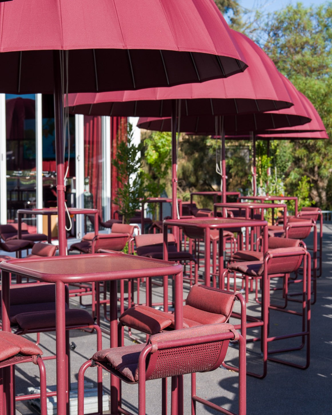 Outdoor seating area with red tables and chairs under large pink umbrellas.