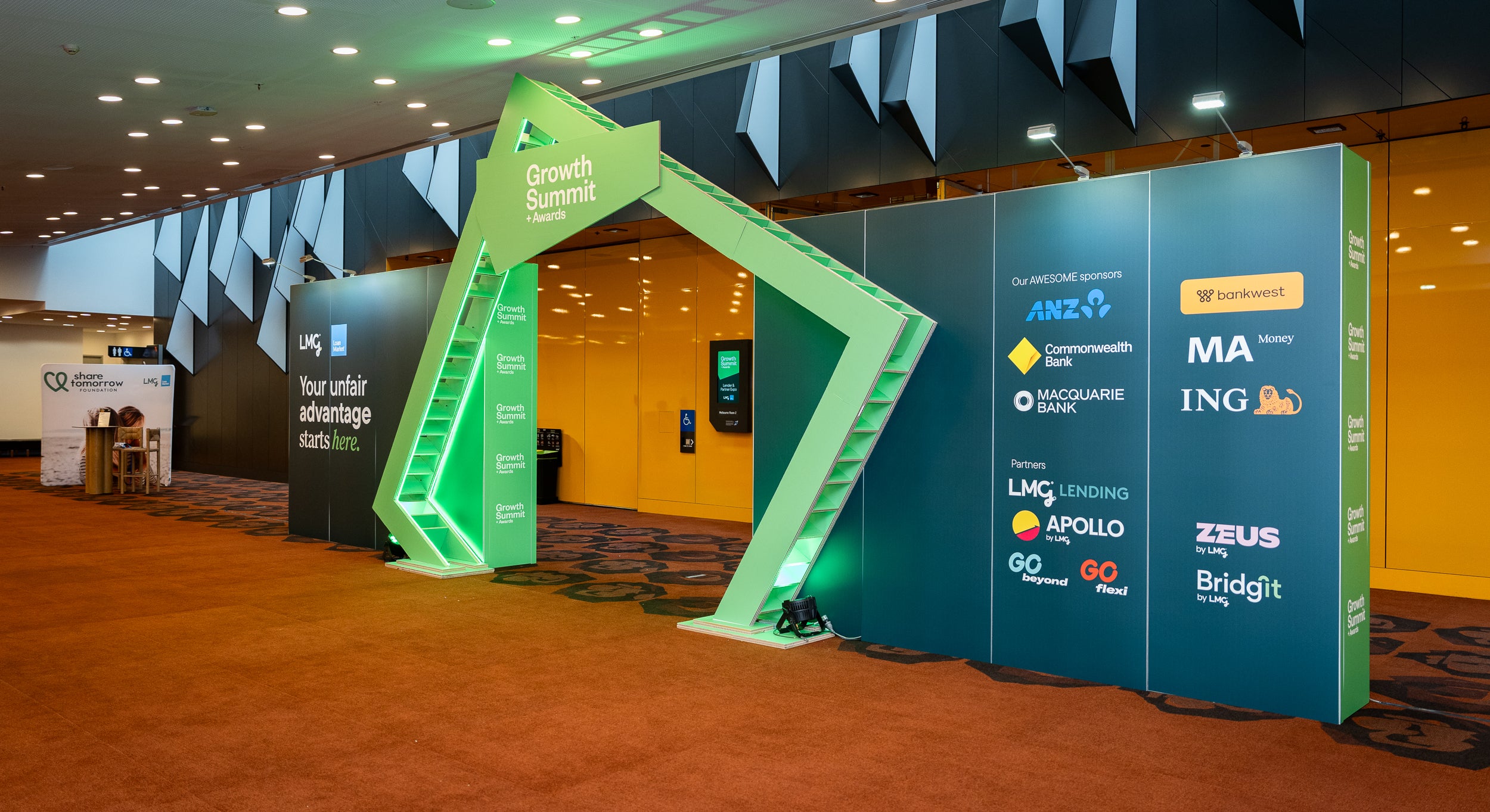 Promotional setup with green and blue arches featuring various brand logos in a conference room. A sustainable signage option
