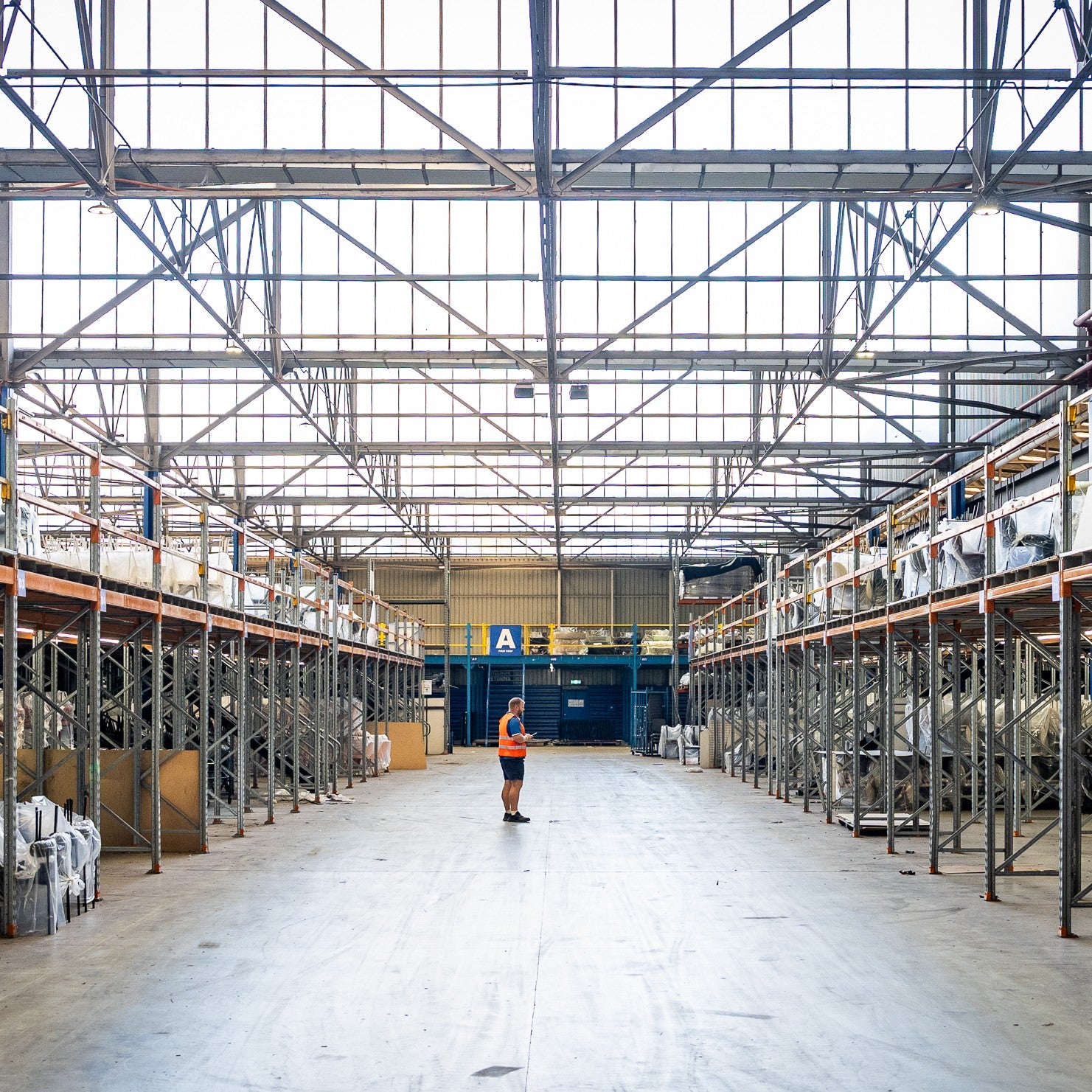 Brooklyn Warehouse employee standing in a large warehouse with high ceilings and metal shelving units.