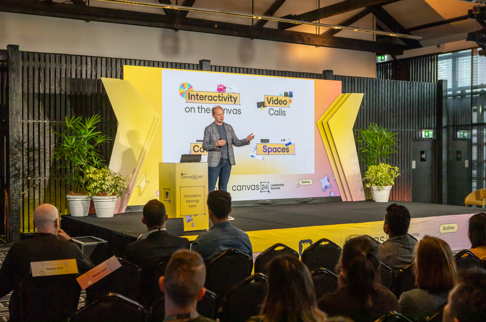 Person giving a presentation on a stage with a large screen displaying 'Canvas' branding.