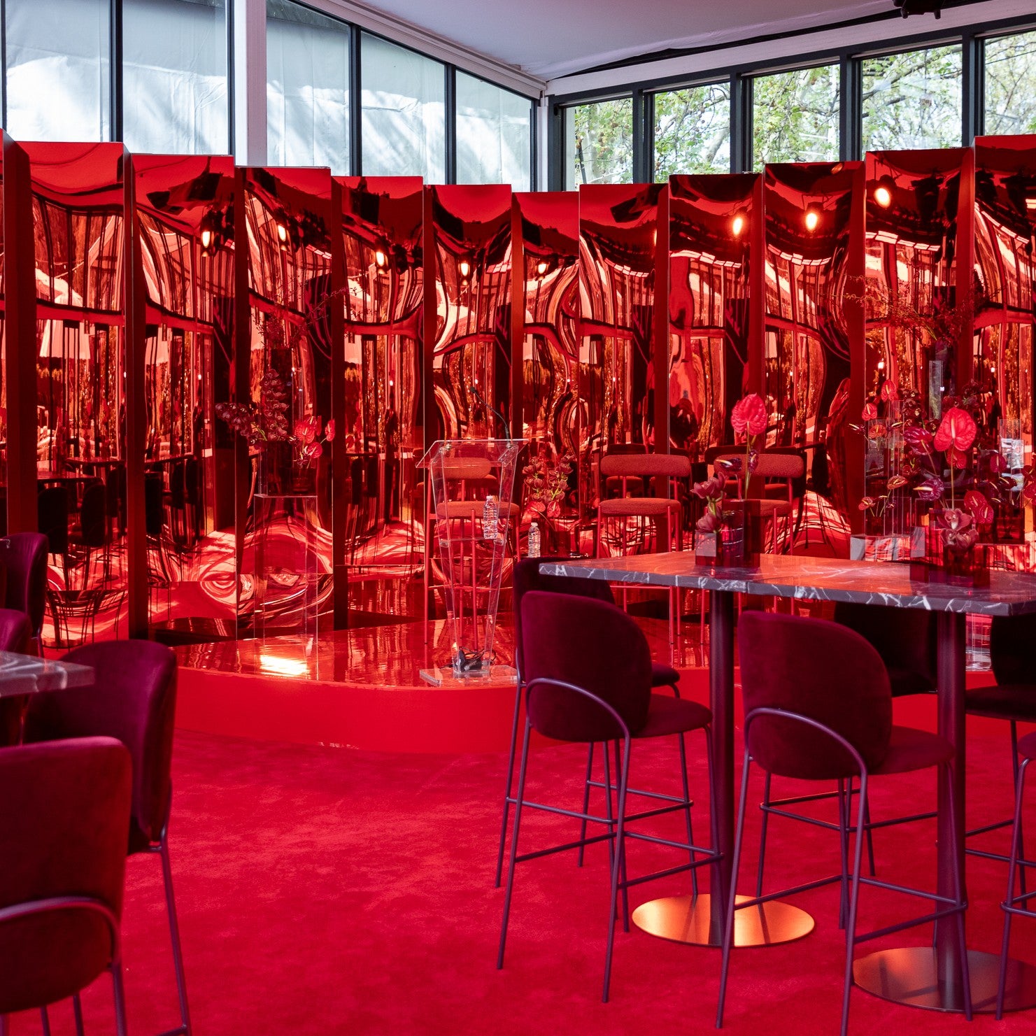 Dramatic event interior bathed in deep red lighting with styled tables and chairs. Onsite at AFL September Club. Pictured: Halo Table, Margot Chairs, Sofia Stools and custom work in our marquee.