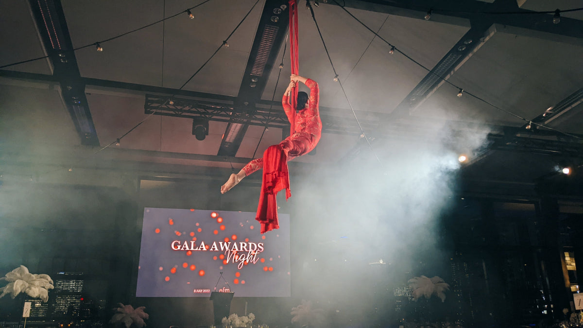 Person in red costume hanging from a rope with 'Gala Awards Night' screen in the background