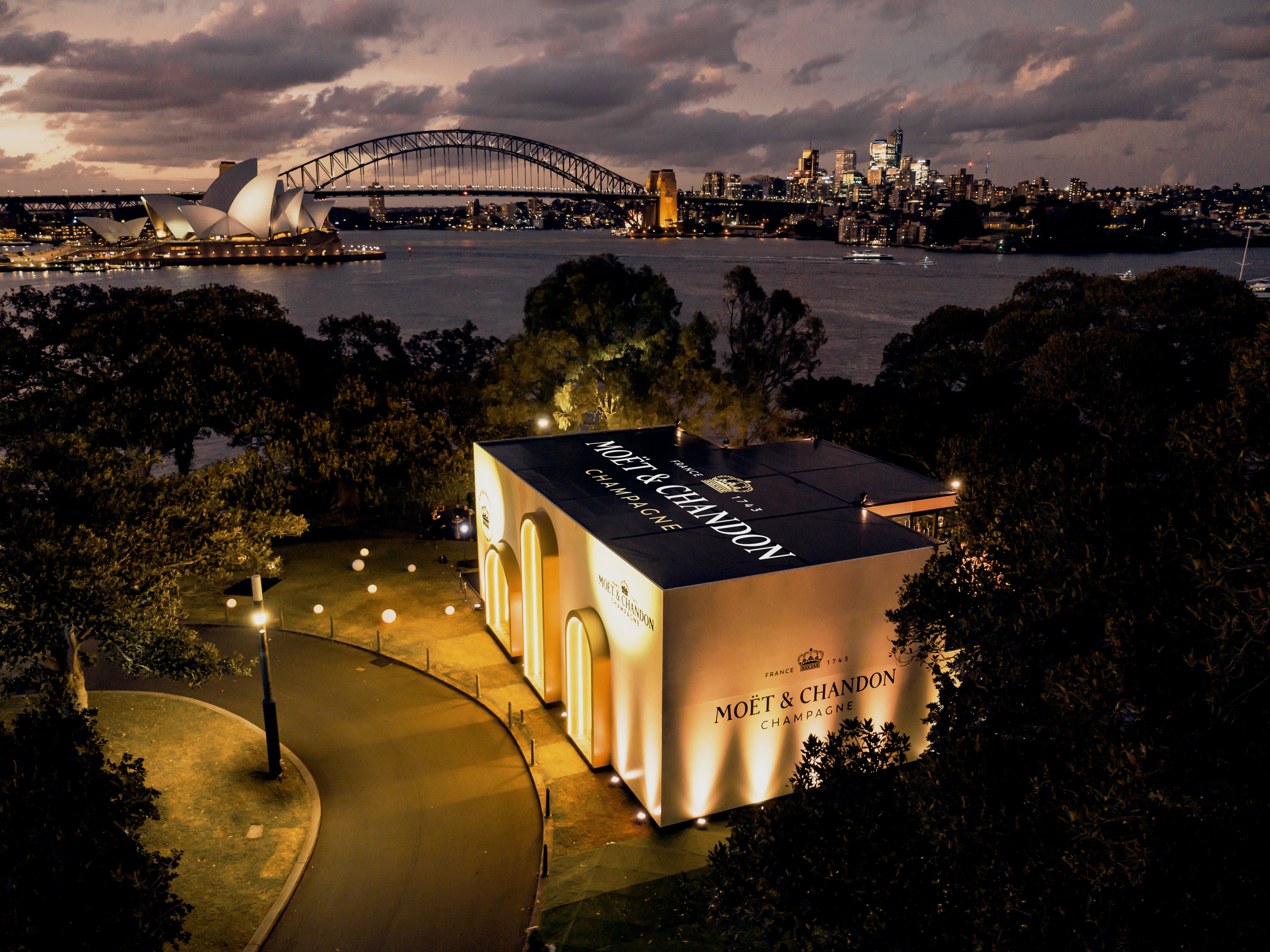 Marquee illuminated with Moet & Chandon branding against a cityscape with a bridge and Opera House.
