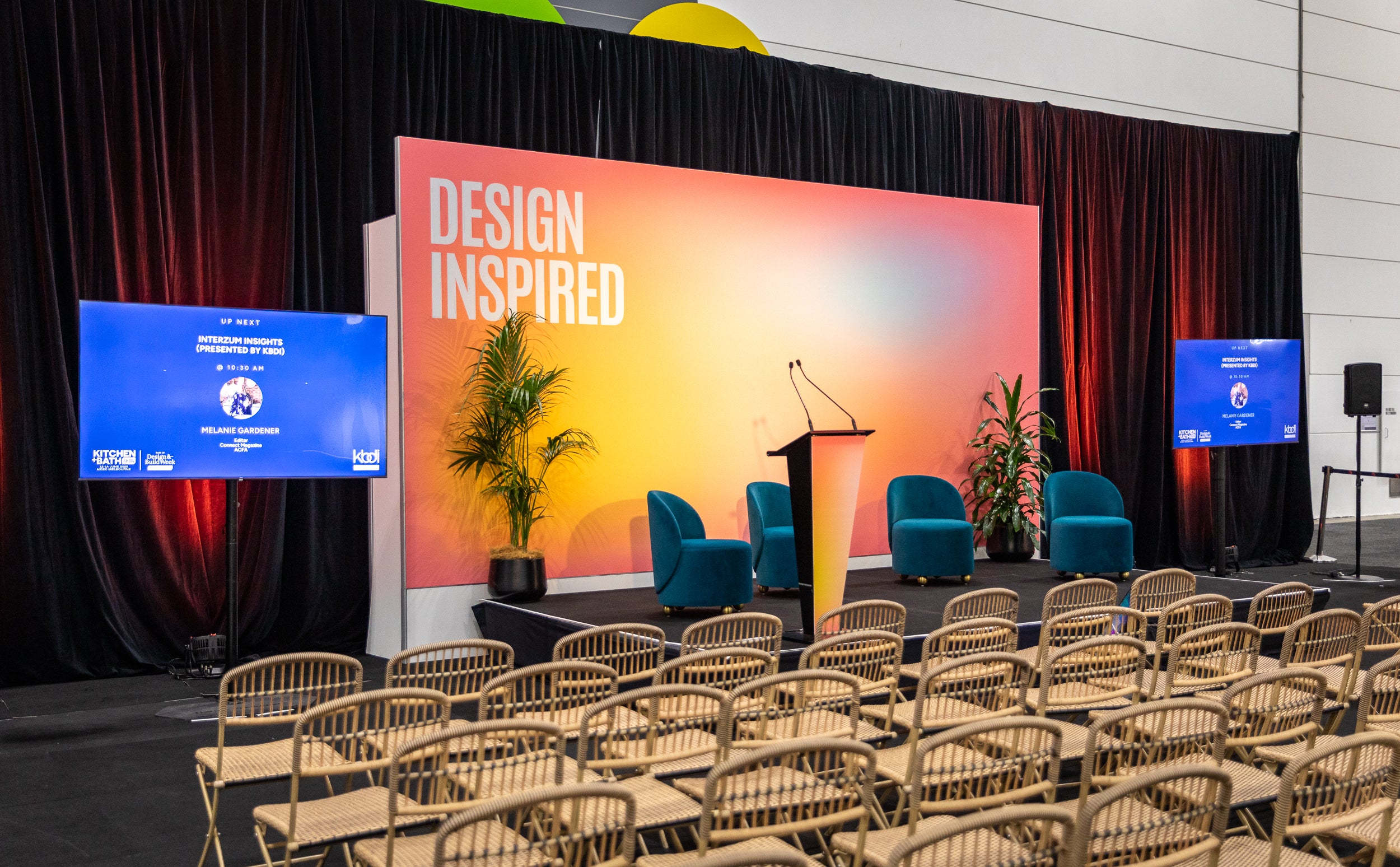 Conference room setup with 'Design Inspired' backdrop and audience chairs.