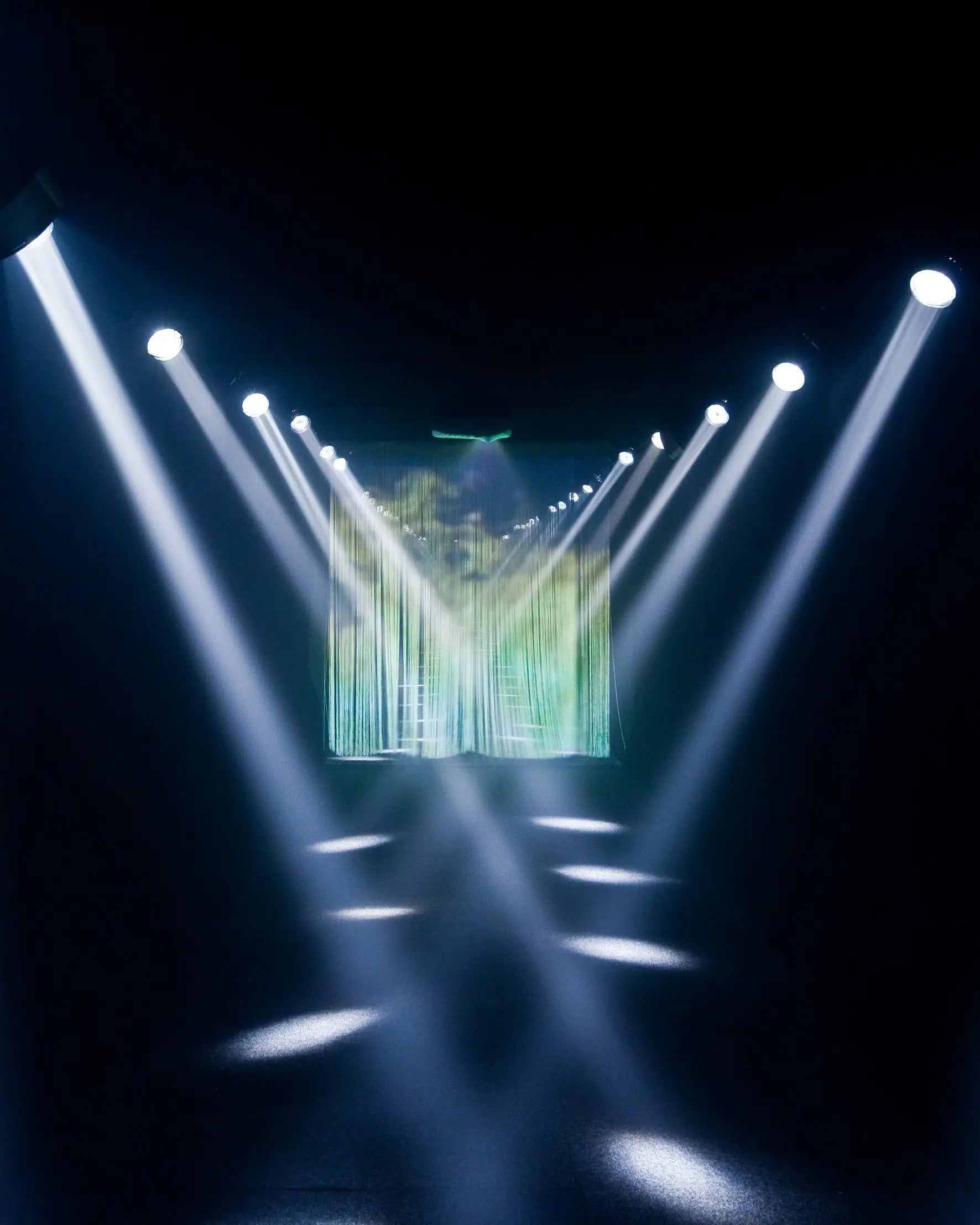 Stage lights with beams pointing towards a screen displaying a digital landscape.