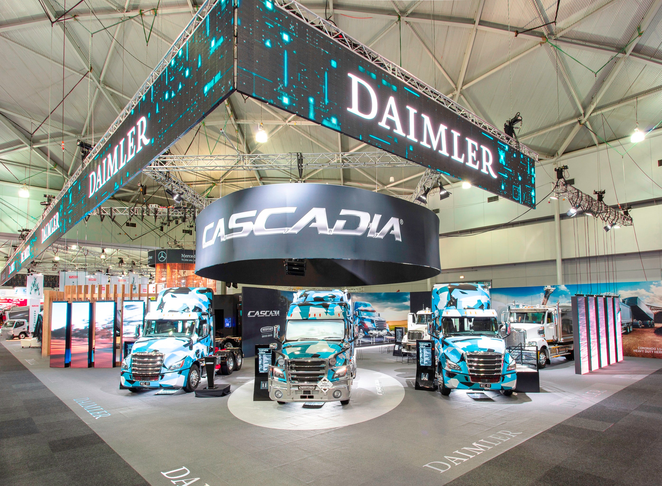 Daimler Cascadia trucks on display at a trade show with branding elements.