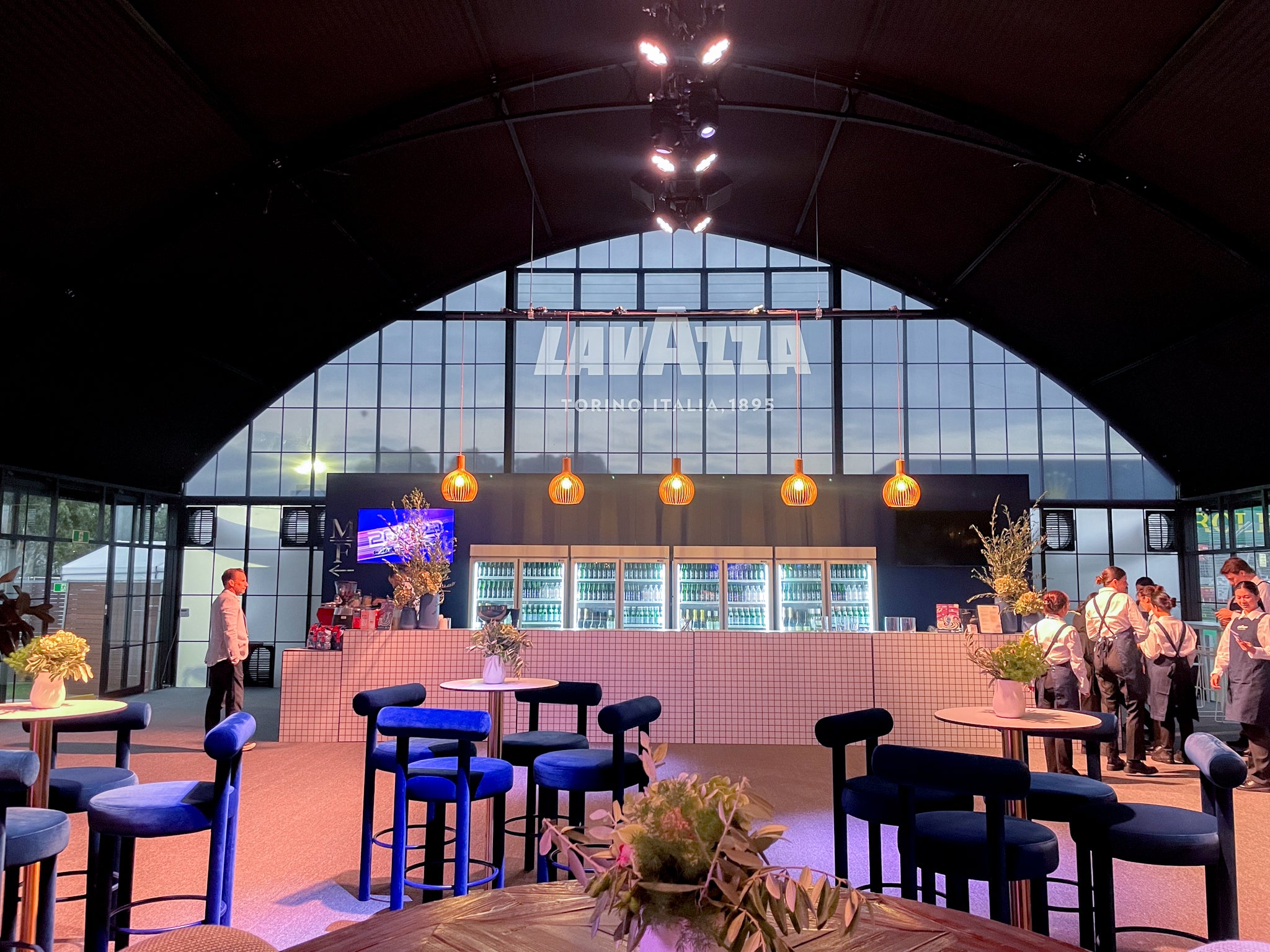 Modern interior with tables, chairs, and a large window displaying the Lavazza logo. Atrium at Australian GP.