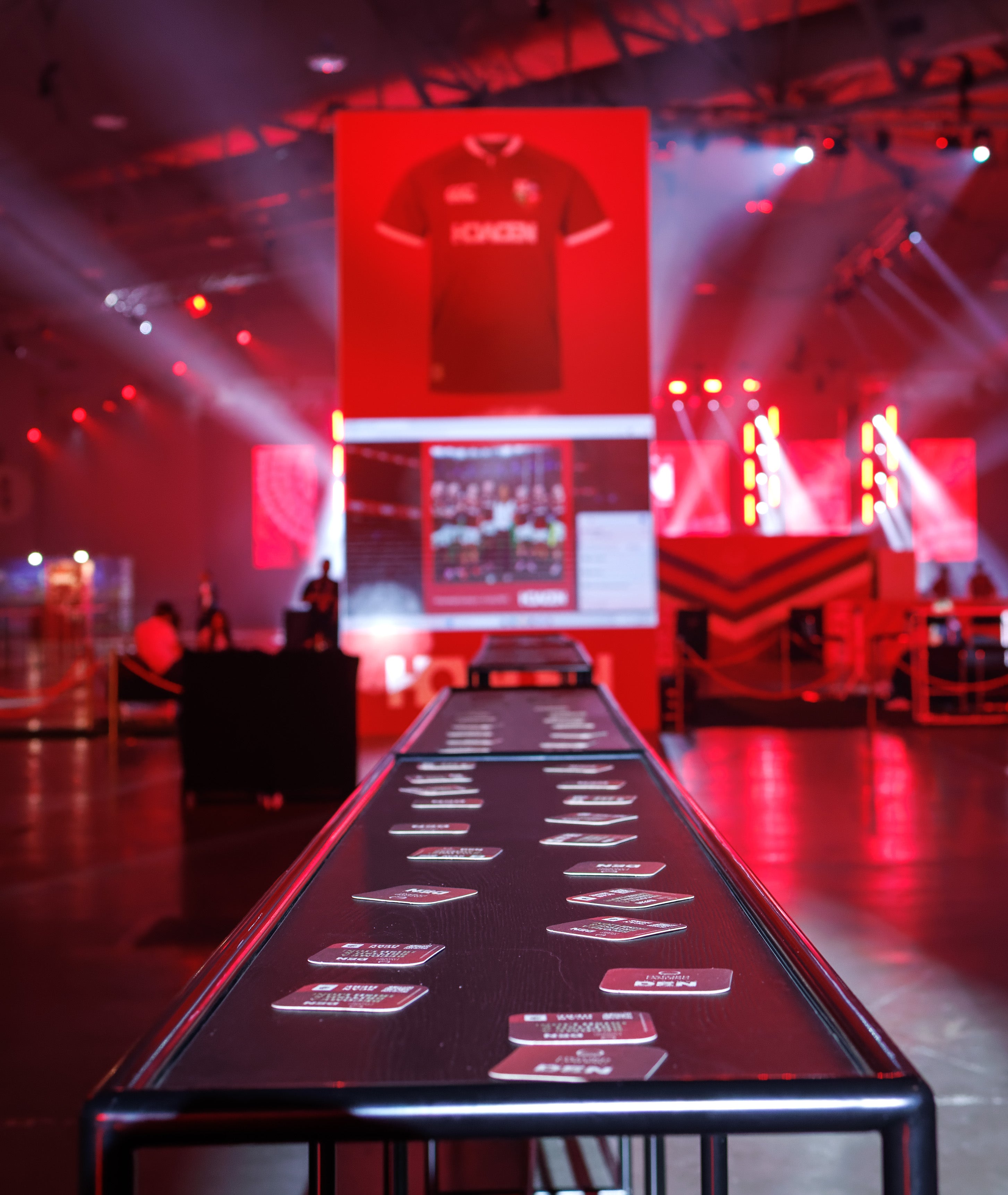 Long Helix table in a red-lit room with a screen displaying a sports jersey.