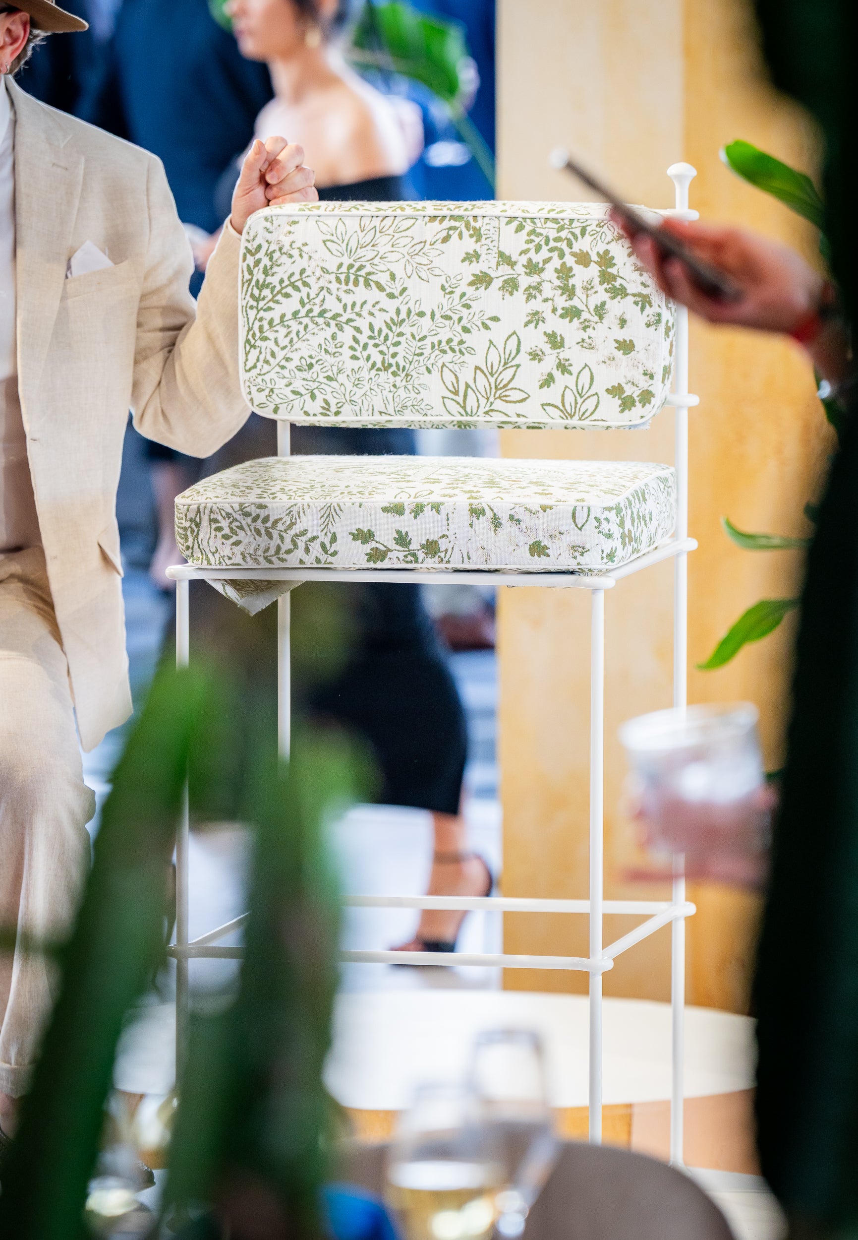 Decorative chair with floral pattern on a stand, blurred people in the background