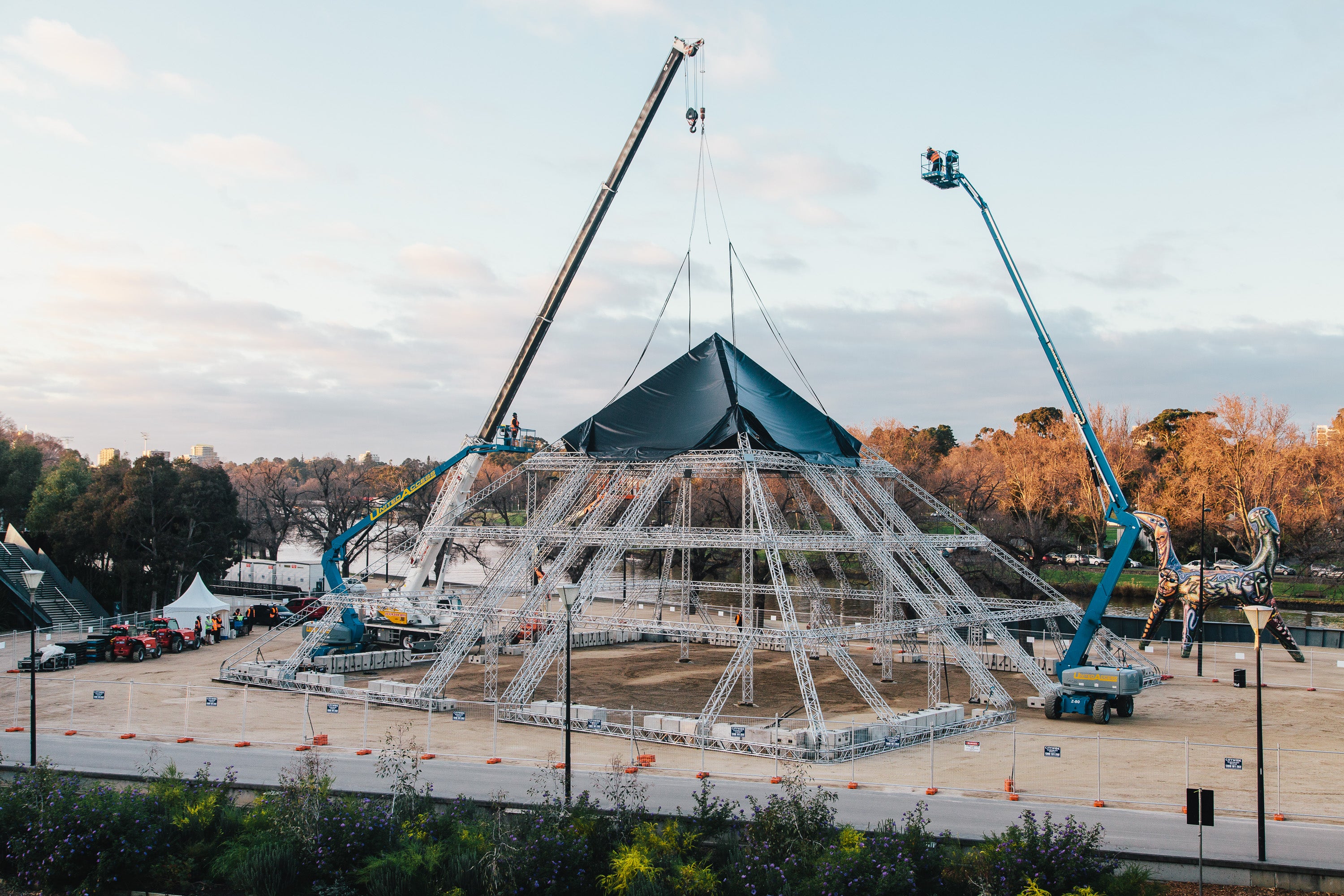 Construction site with a large geometric structure being assembled using cranes.