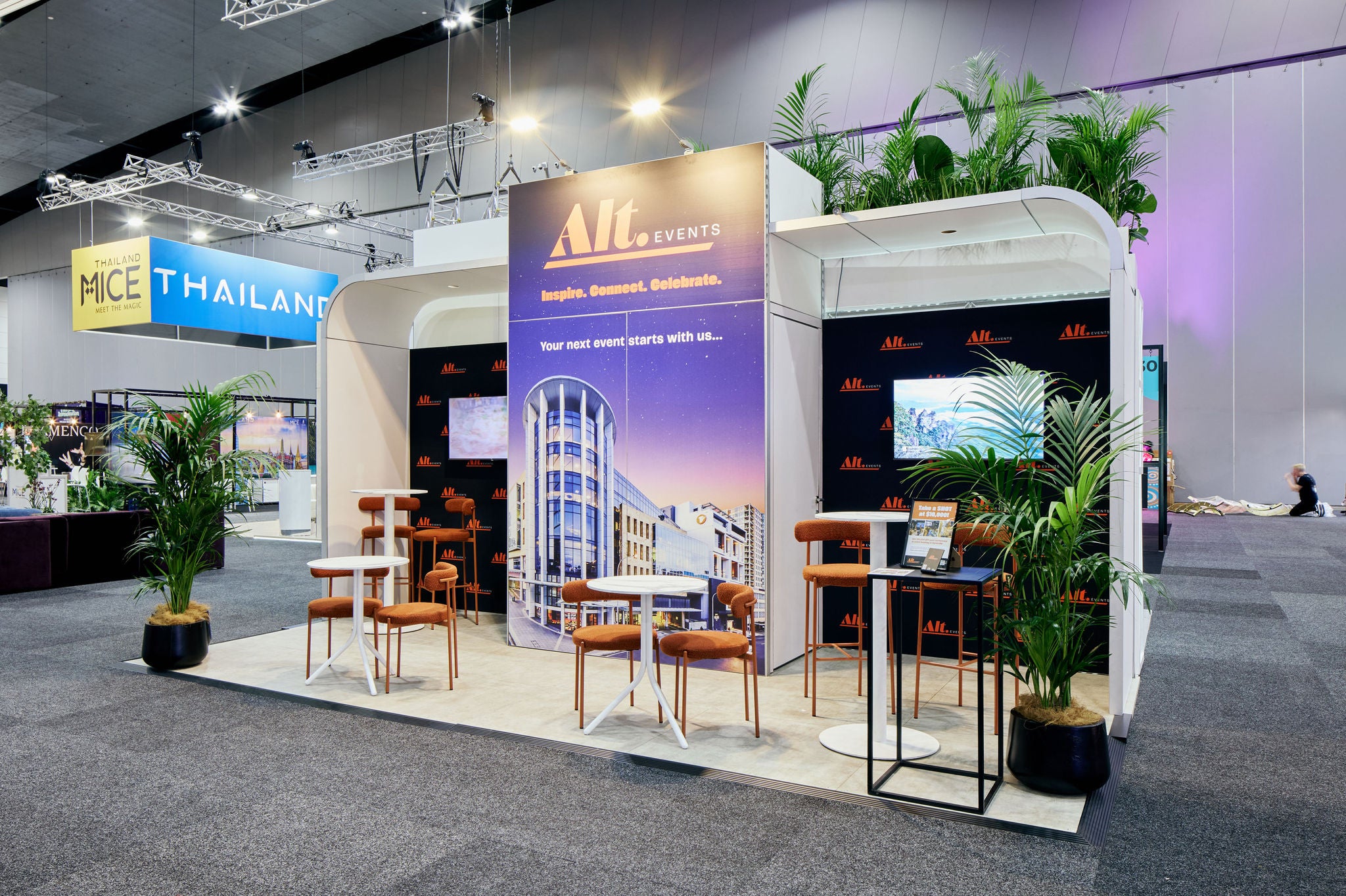 Exhibition stand with branding at a trade show, featuring chairs and plants.