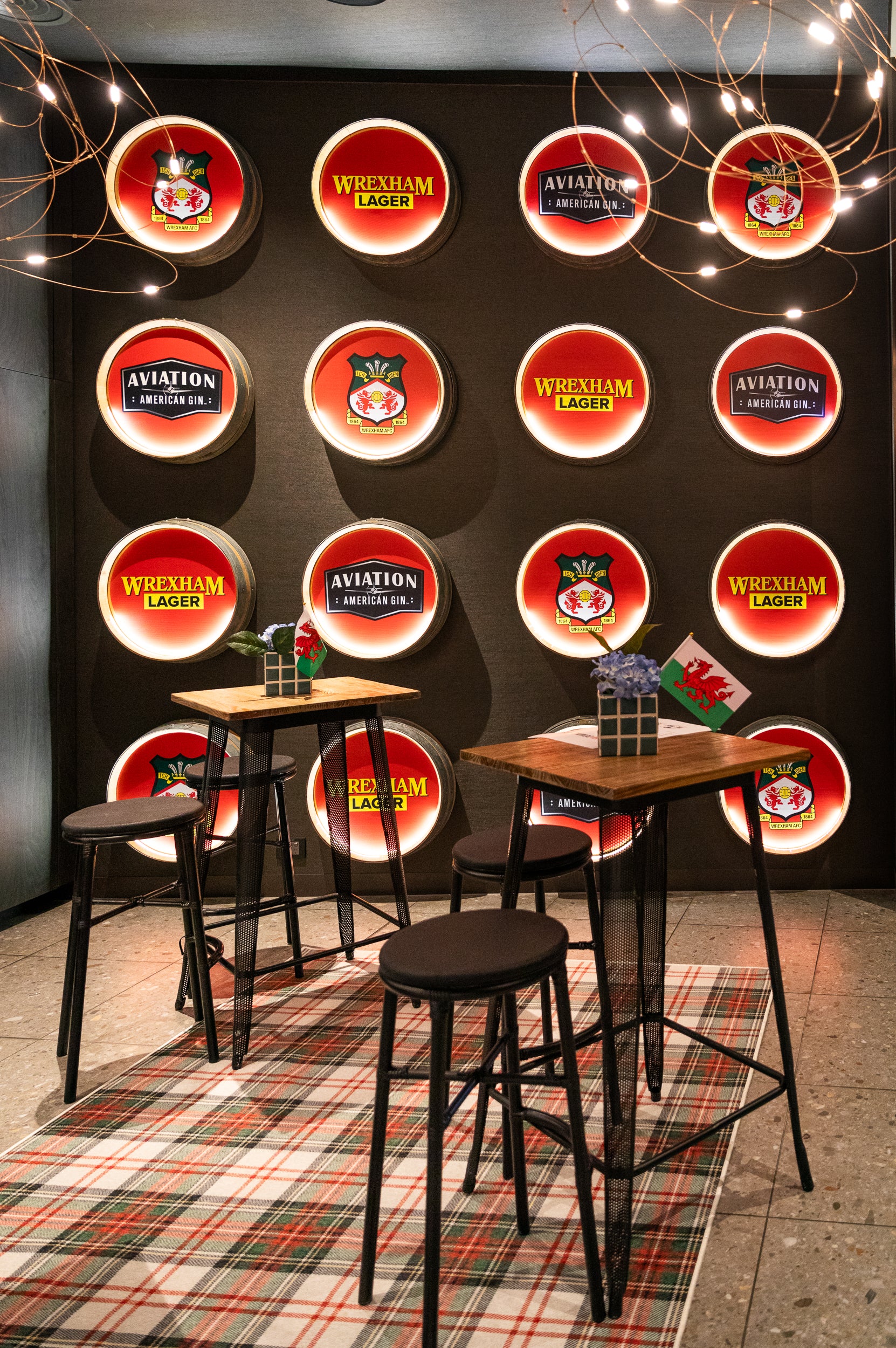 Bar area with high tables and stools against a wall with branded circular signs from Wrexham.