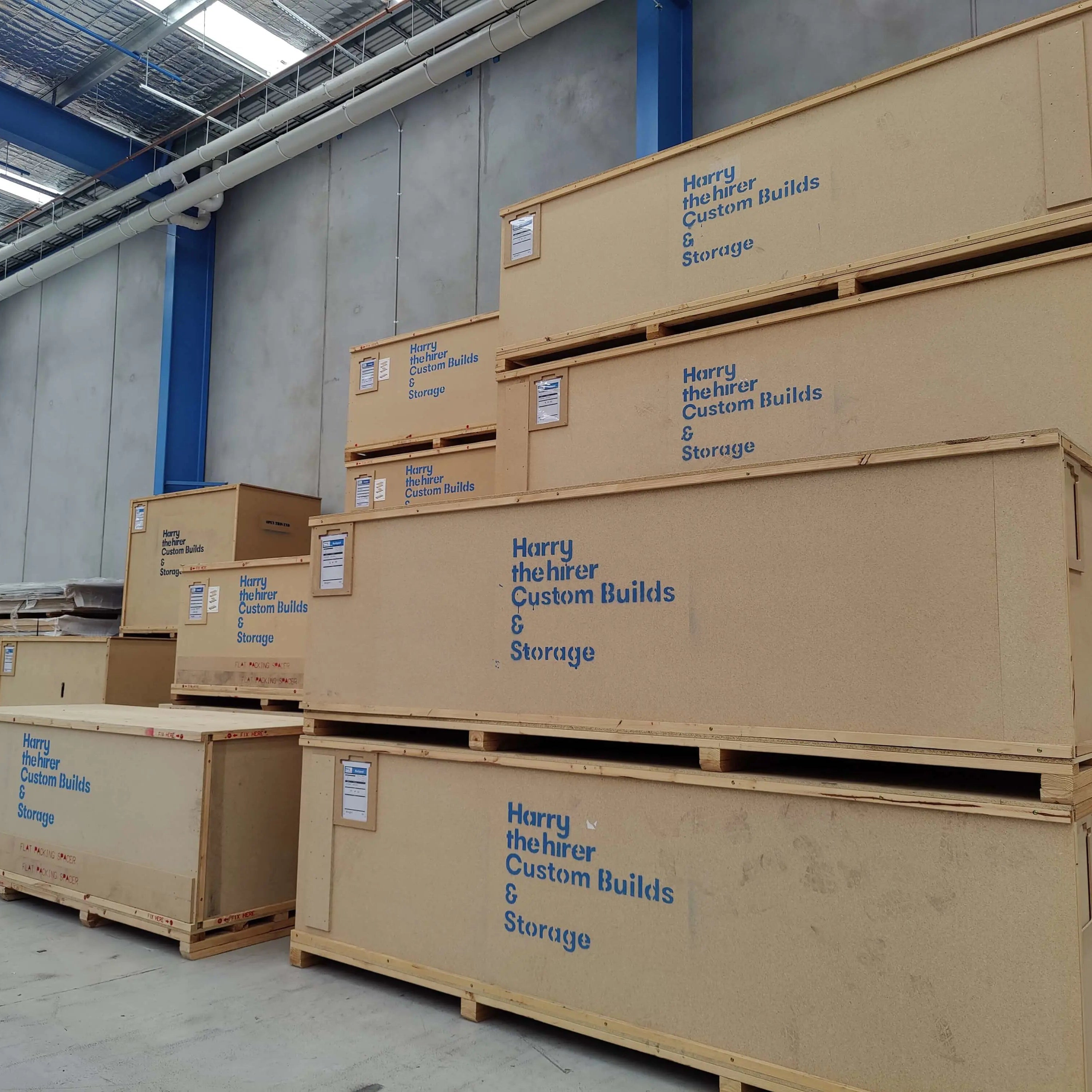 Stack of brown storage containers with 'Harry The Hirer Custom Builds & Storage' branding in a warehouse.