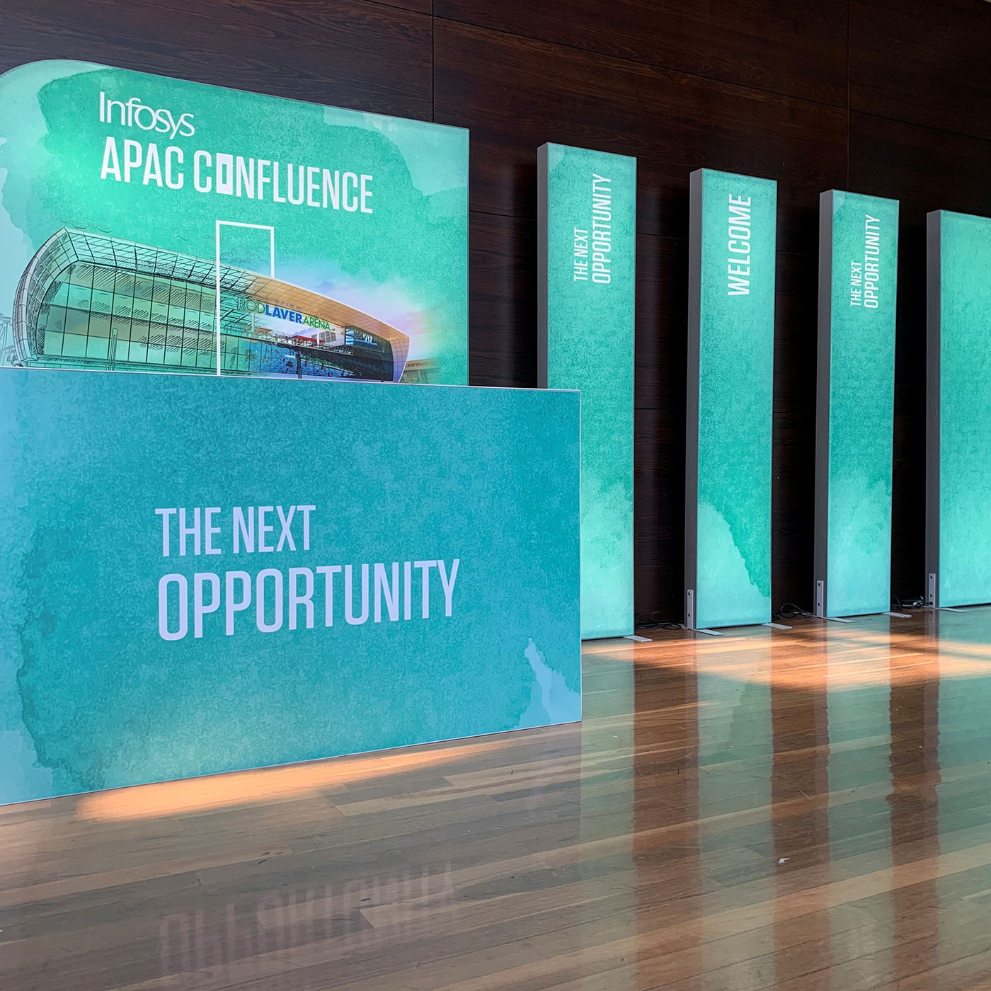 Teal display panels with 'Infosys APAC Confluence' branding and 'The Next Opportunity' text in a room.