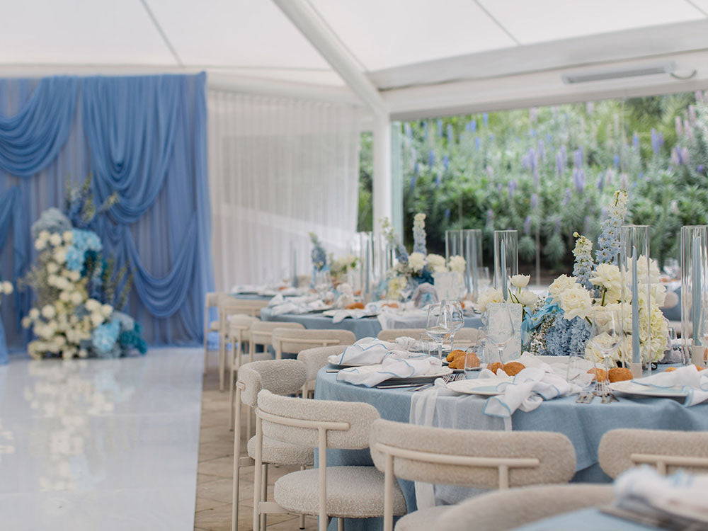 Decorated event space with tables set for a private event, featuring blue and white color scheme. Featuring our Margot chairs