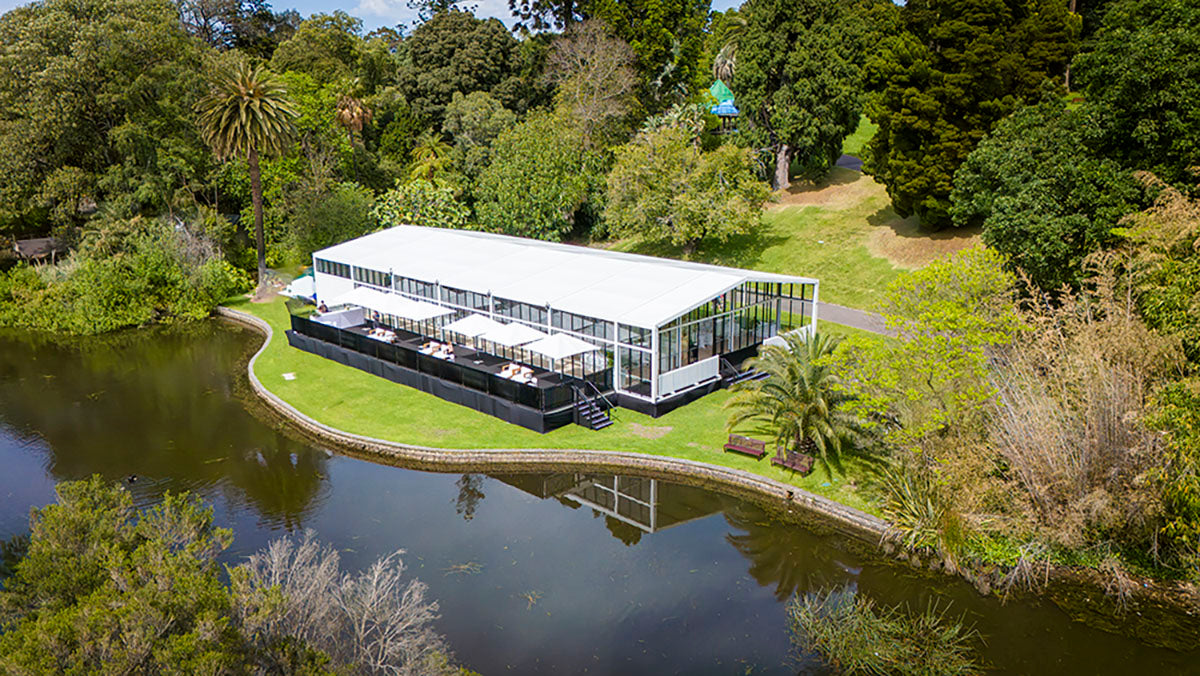 Alto structure with white roof and black exterior surrounded by greenery and a lake