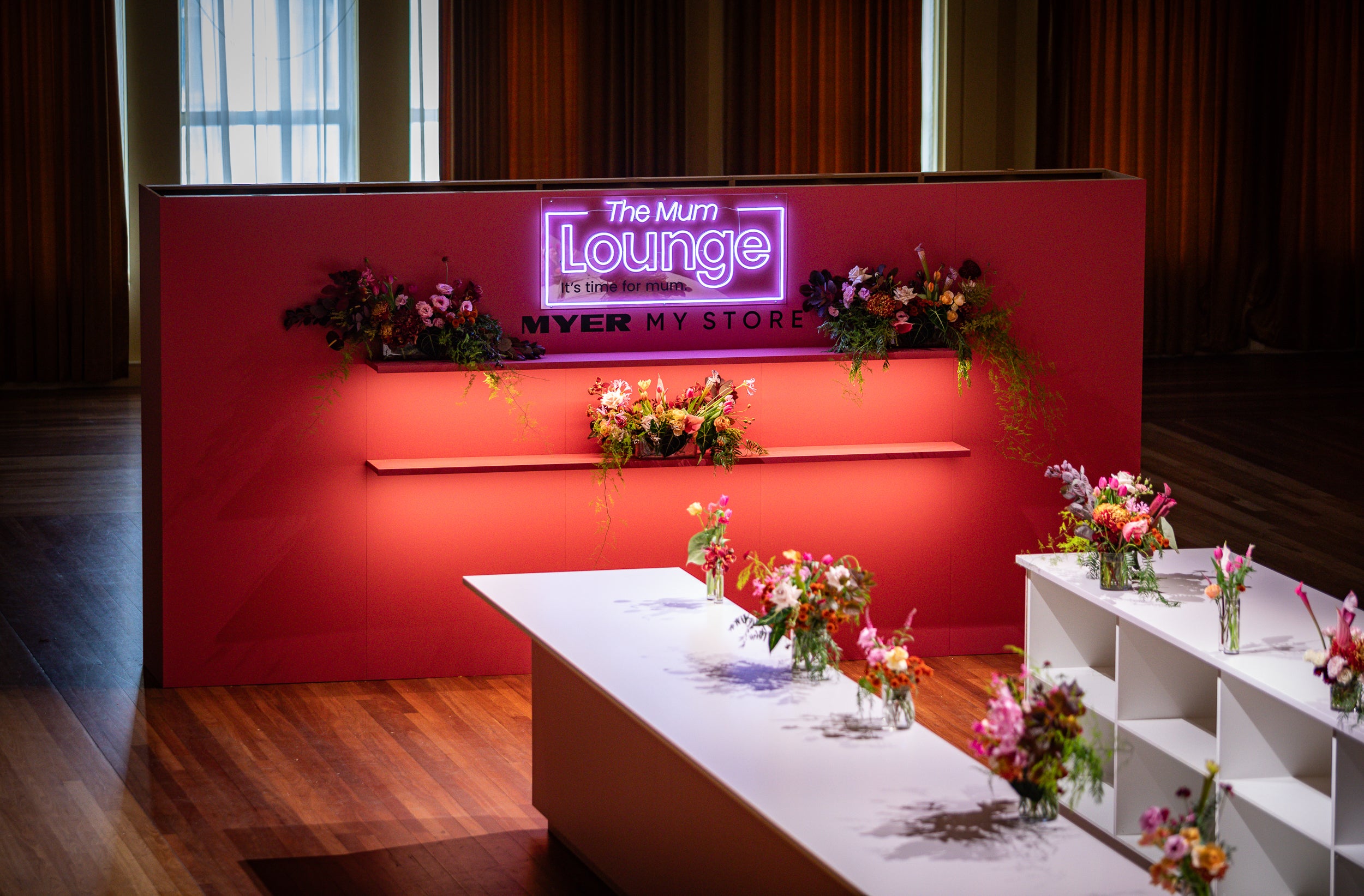 Neon sign for 'The Mum Lounge' with floral arrangements on a red wall for a Myer brand activation