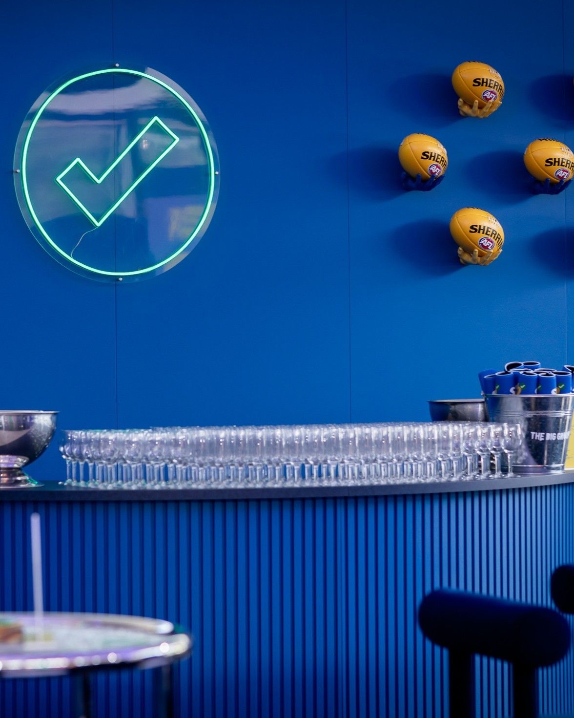 Bar setup with clear glasses, a blue wall, and sports balls with logos.