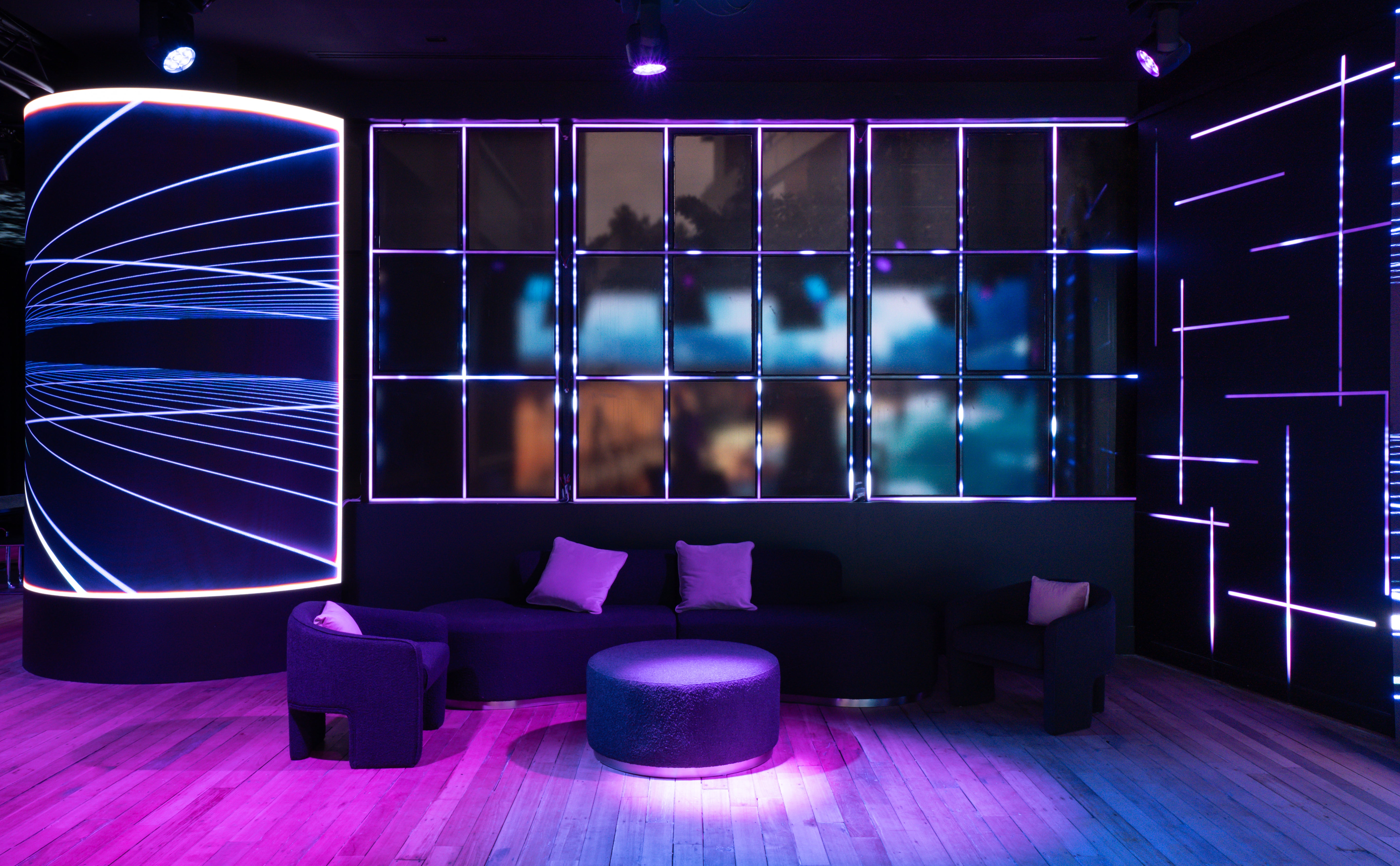 Modern interior with purple lighting, round ottoman, and decorative wall panels.