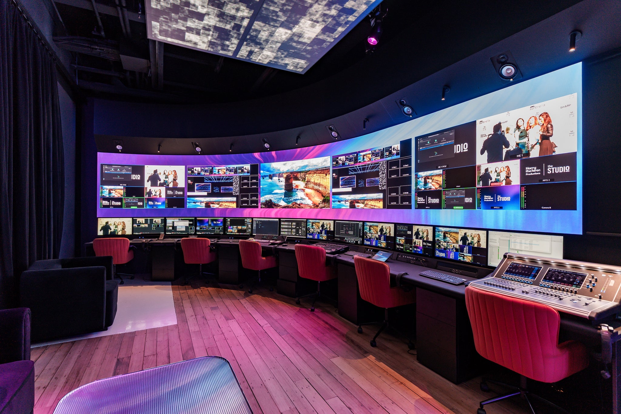 Control room with multiple monitors displaying various scenes, red chairs, and a control panel in our Abbotsford Studio