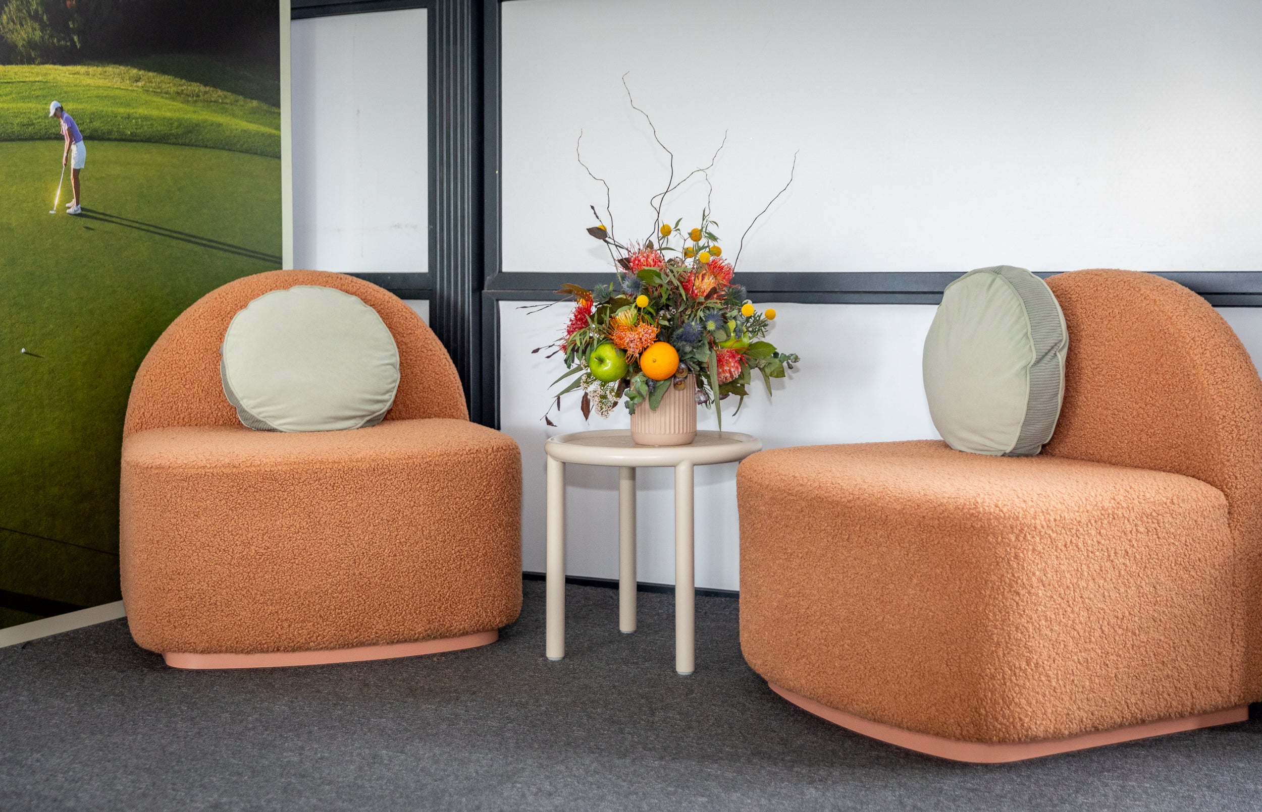 Two orange Harper chairs with a small table and floral arrangement in an indoor setting.