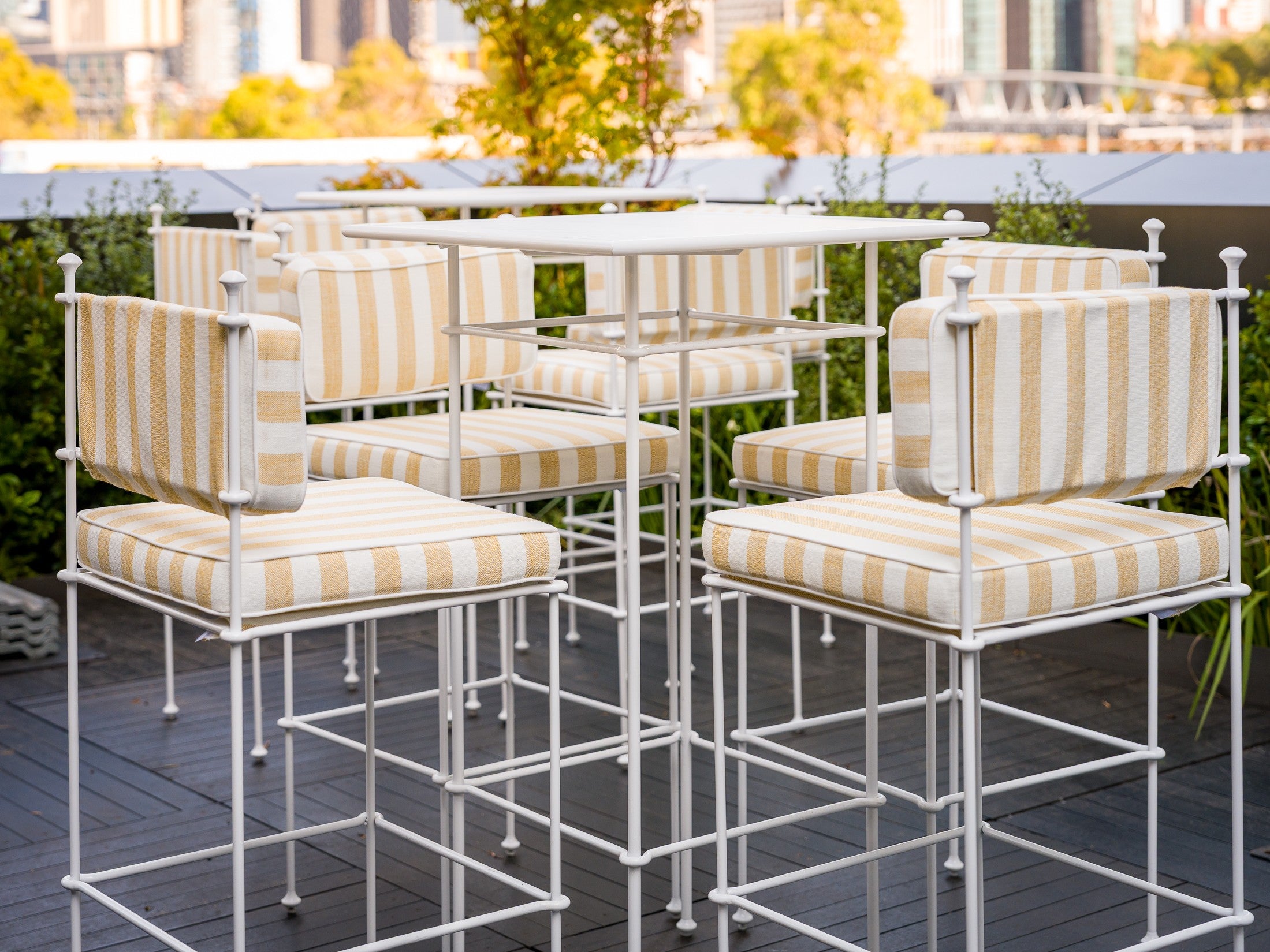 Outdoor furniture set with striped chairs and tables on a rooftop with cityscape background. Pictured: Gigi Range