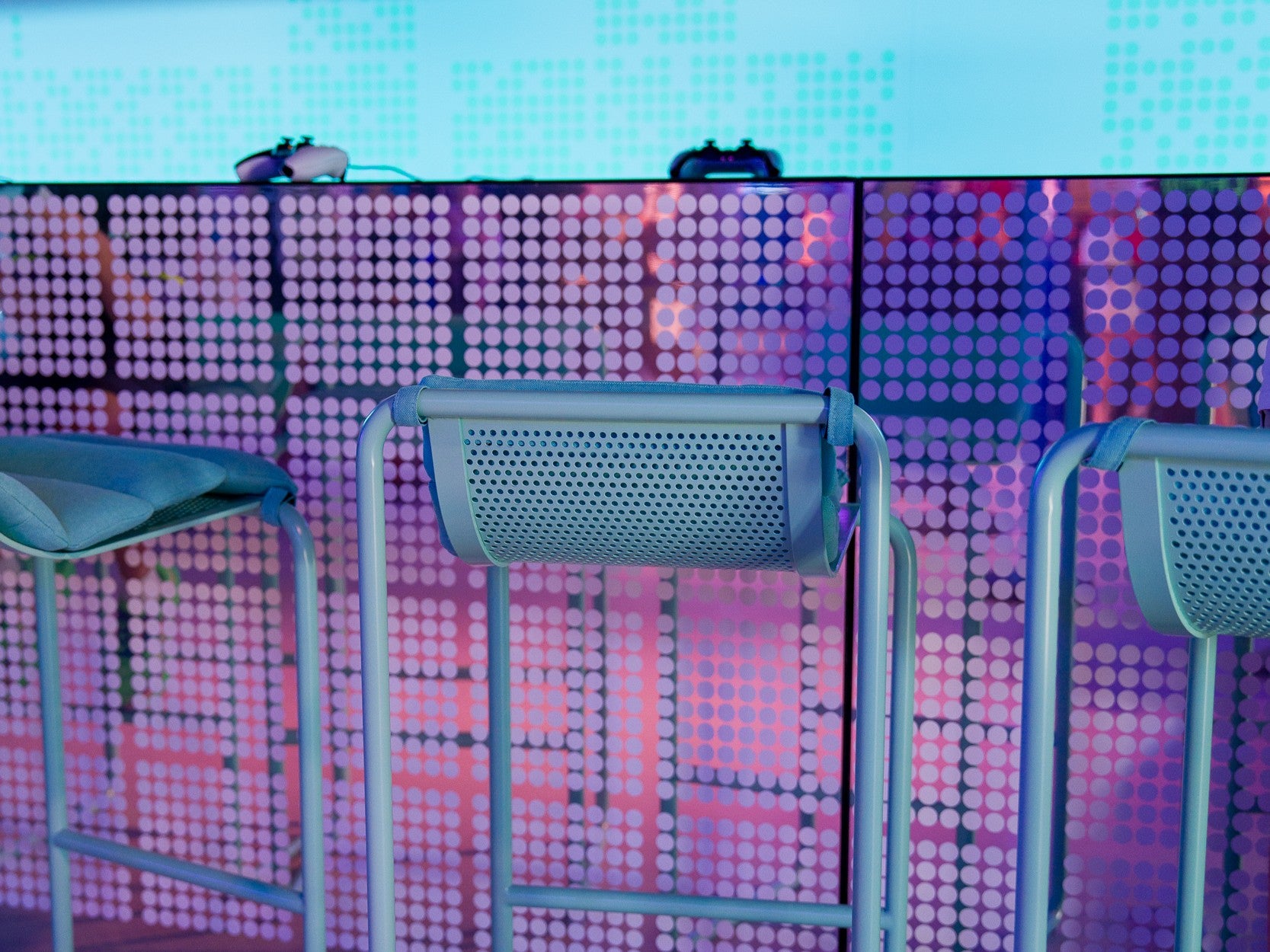 Three blue stools in front of a colorful LED screen with pink and purple patterns.