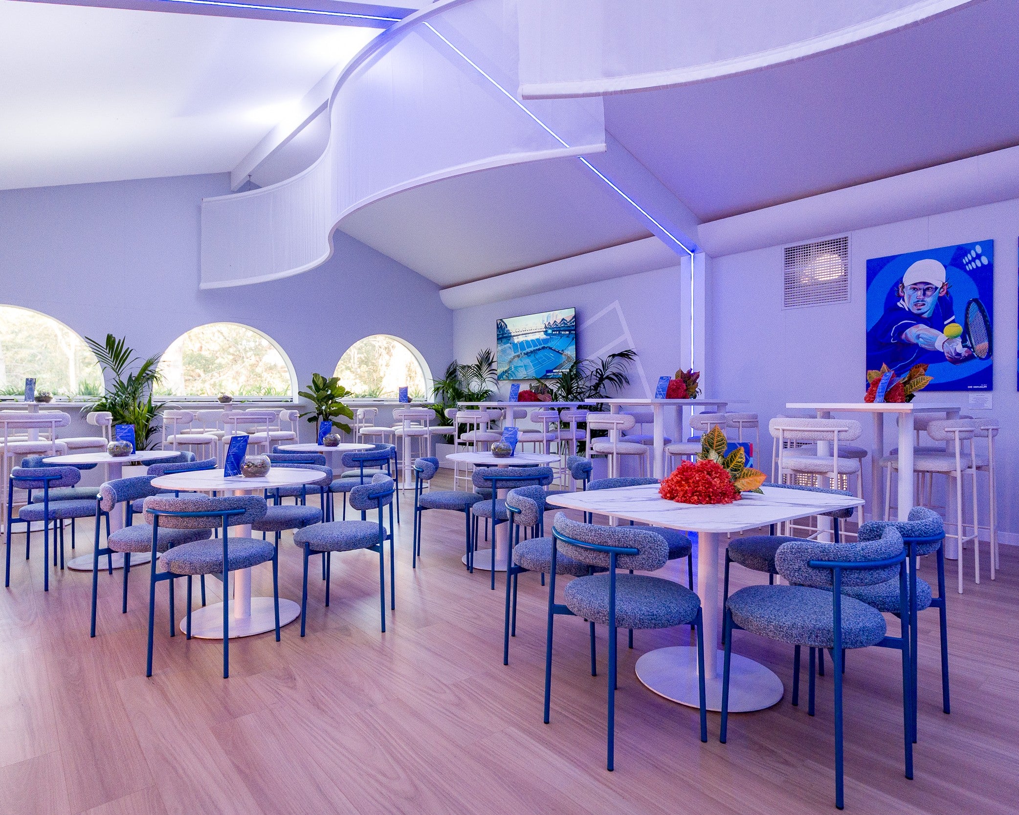 Marquee interior with blue chairs and white tables, featuring a TV screen on the wall.