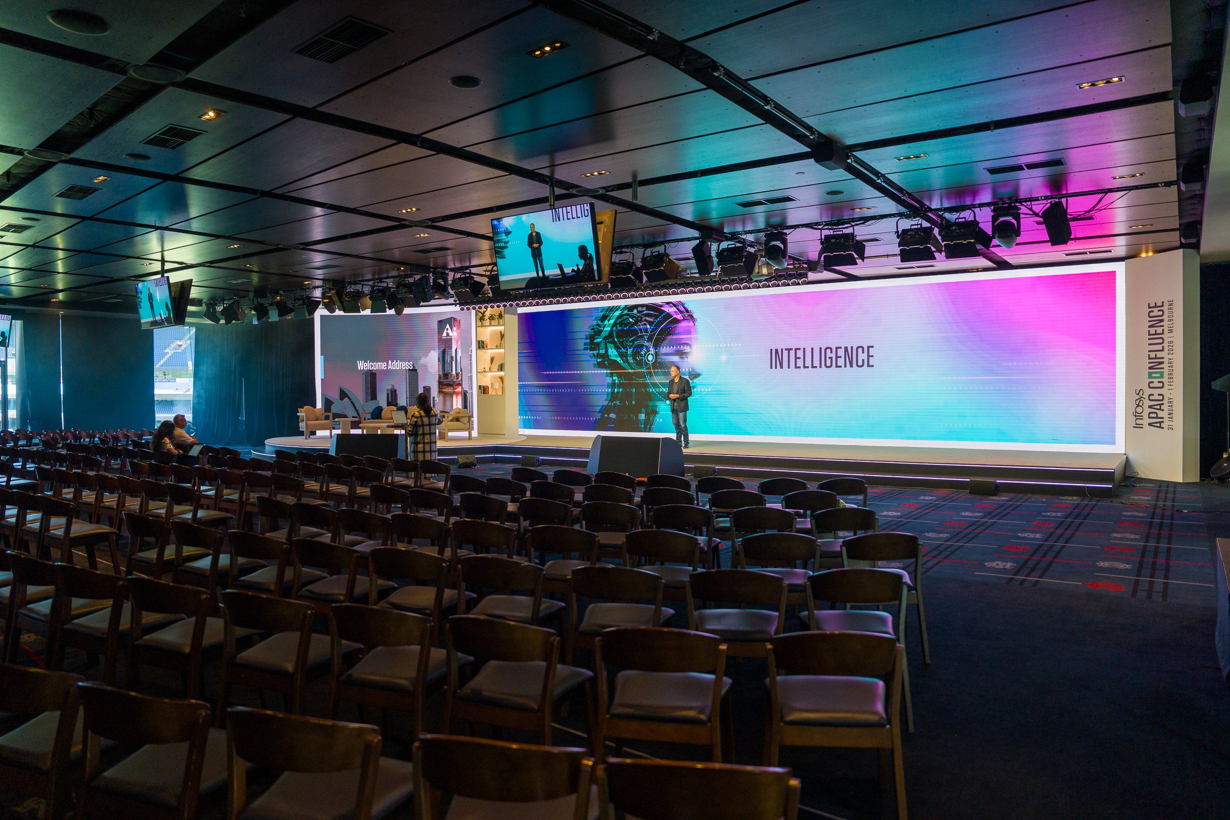 Large conference room with a stage and large screens displaying 'Intelligence' theme.