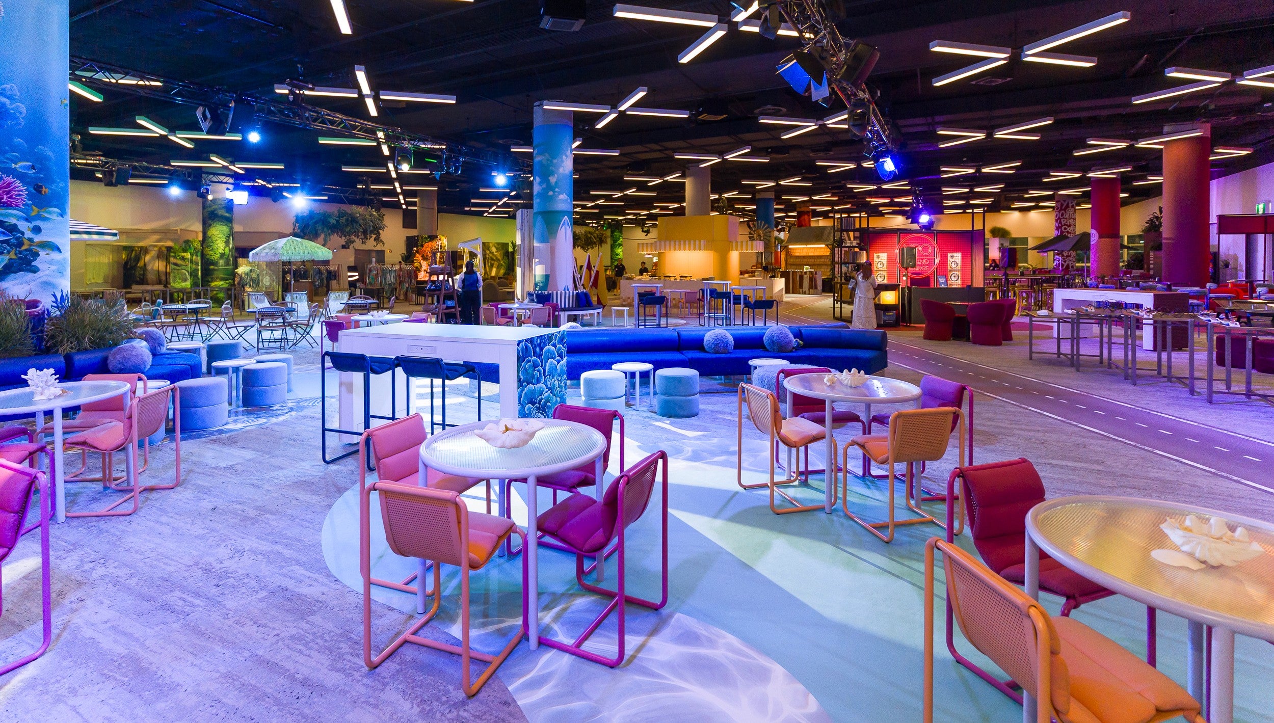 Modern exhibition lounge area with colorful furniture and a central bar area.
