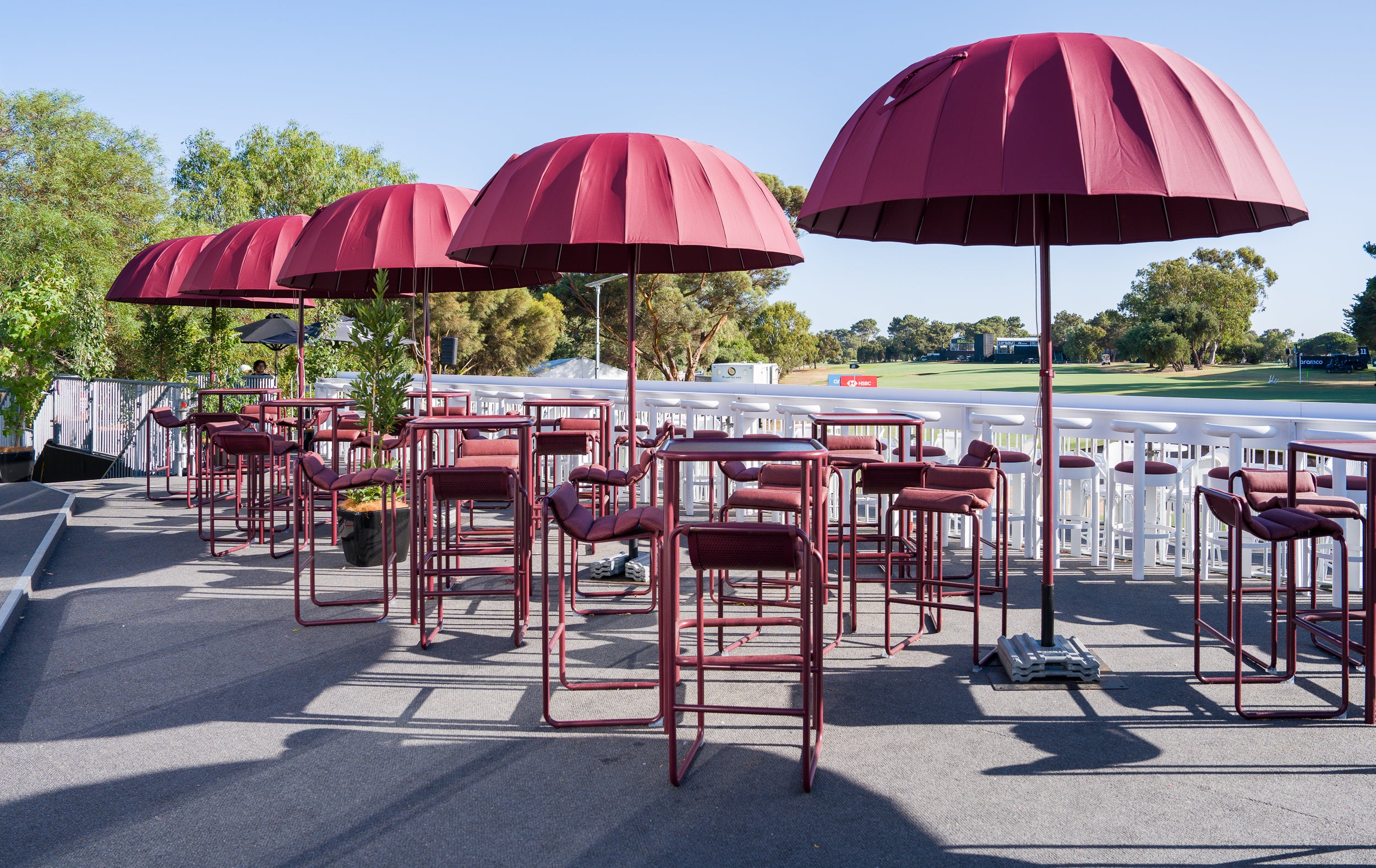 Outdoor seating area with burgundy Isla tables, chairs and umbrellas on a sunny day. Pictured: Liv Golf, Adelaide