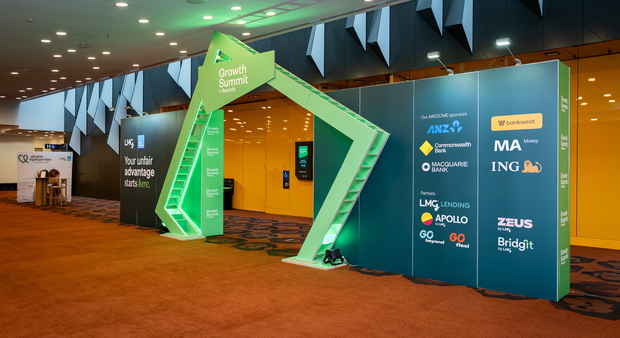 Promotional setup with green and blue arches featuring various brand logos in a conference room. A sustainable signage option