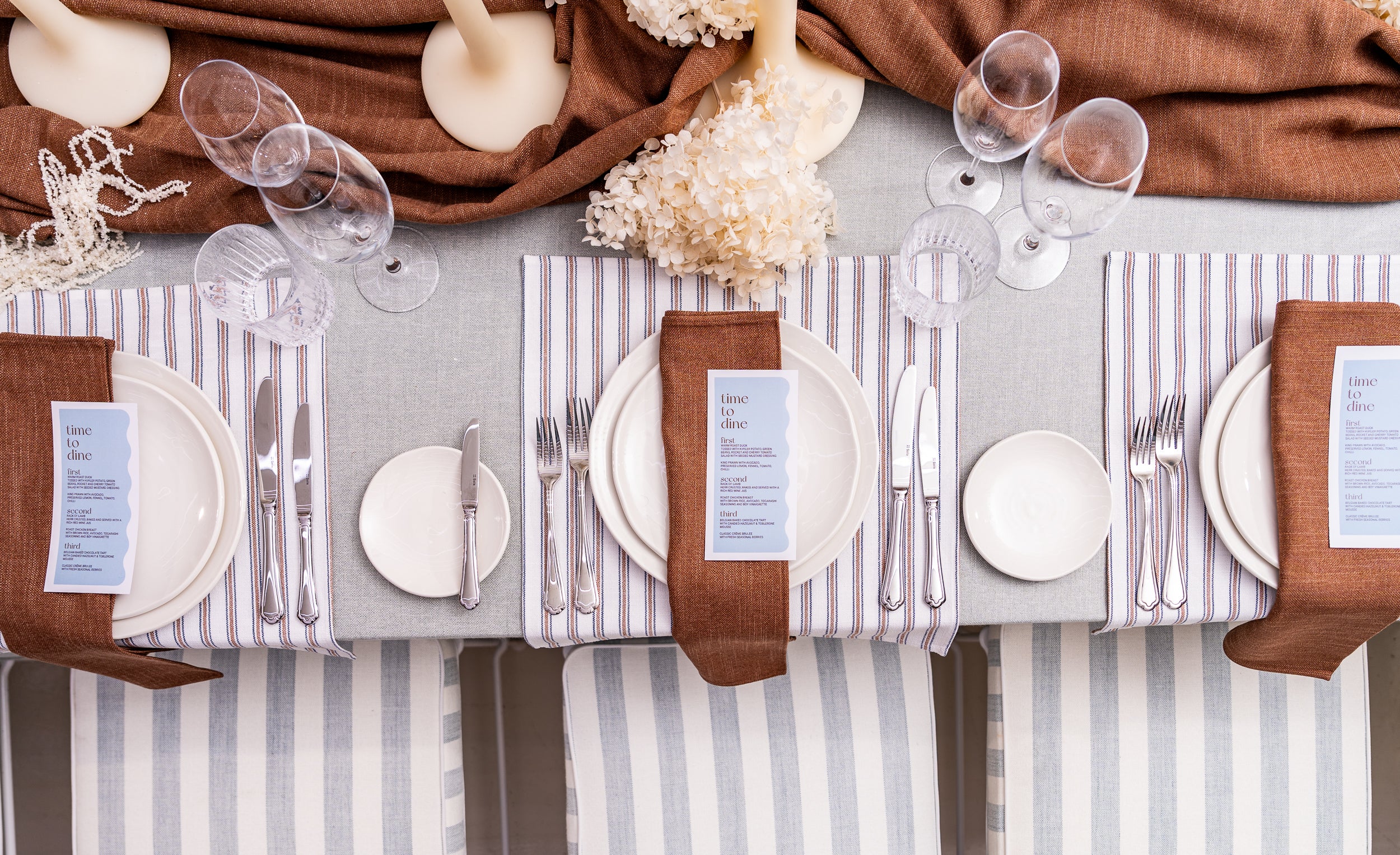Coastal inspired table setting with striped tablecloth, brown napkins, and white plates.