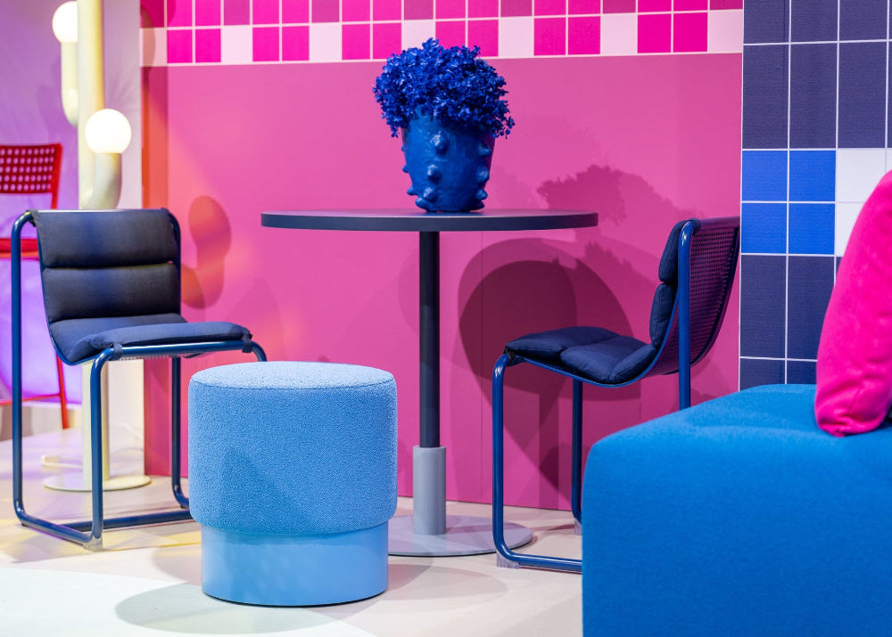 Modern outdoor furniture hire with blue chairs, a blue ottoman, and a pink wall with geometric patterns in our Abbotsford Showroom