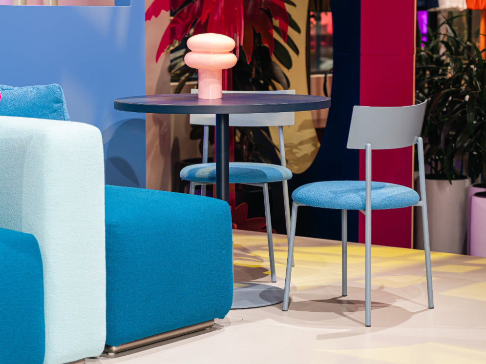 Modern interior with a blue sofa, pink cushions, and a small round table with a pink lamp.