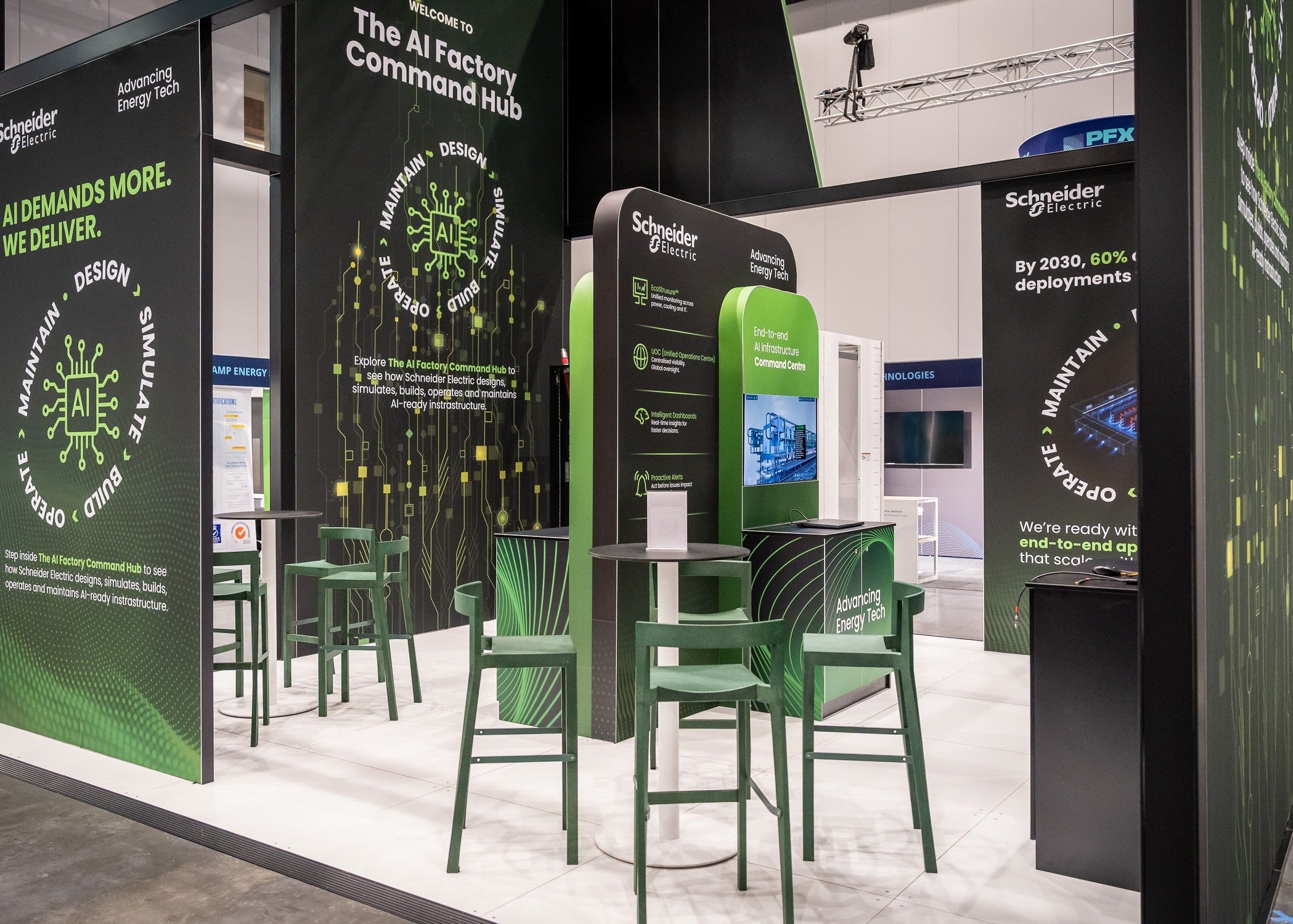 A Schneider Electric branded exhibition booth at a trade show, featuring dark green and black display panels with white and yellow text, green chairs, and small round tables on a light floor.