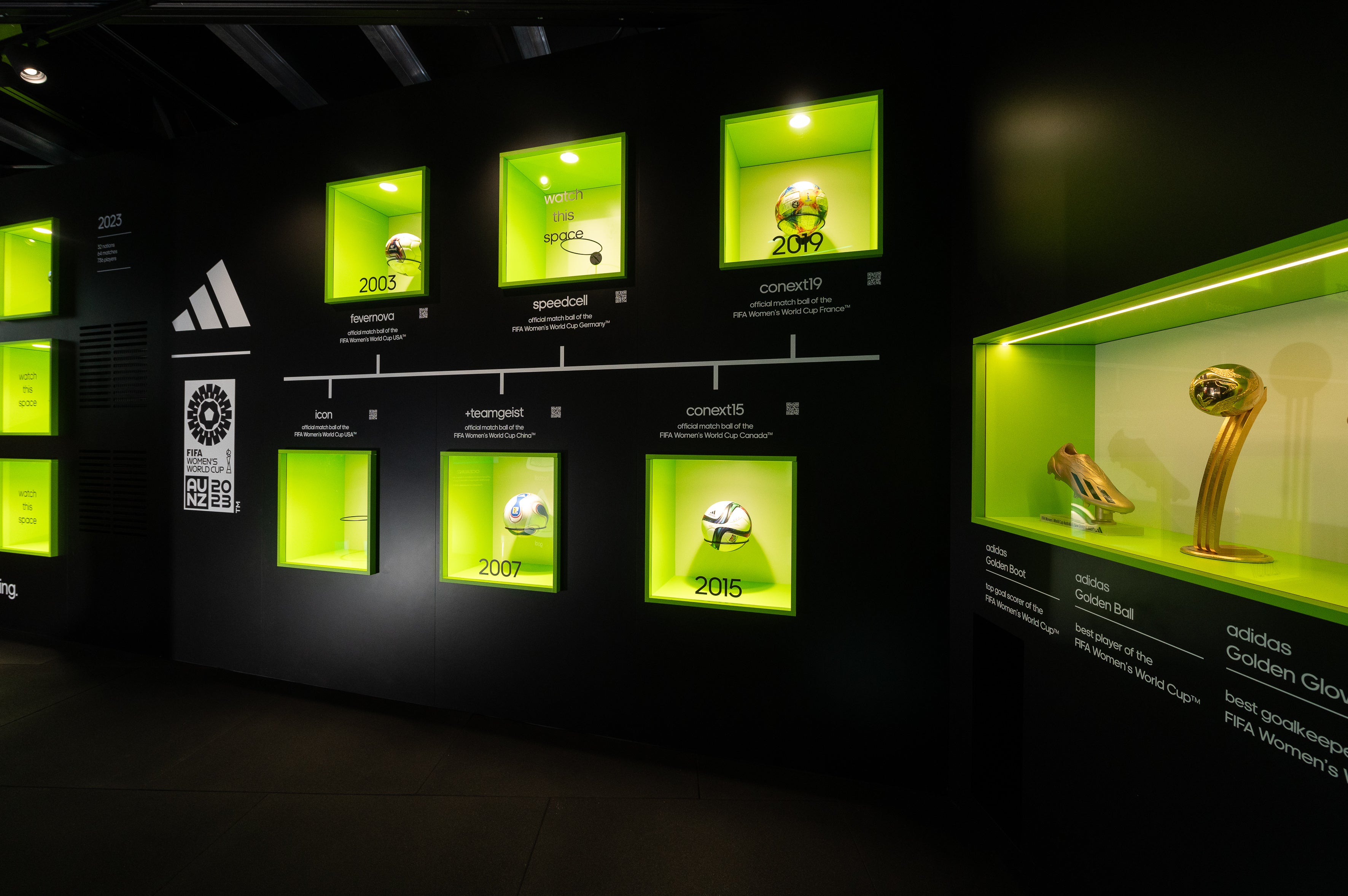 Display case with soccer balls and trophies in a dark room with green lighting