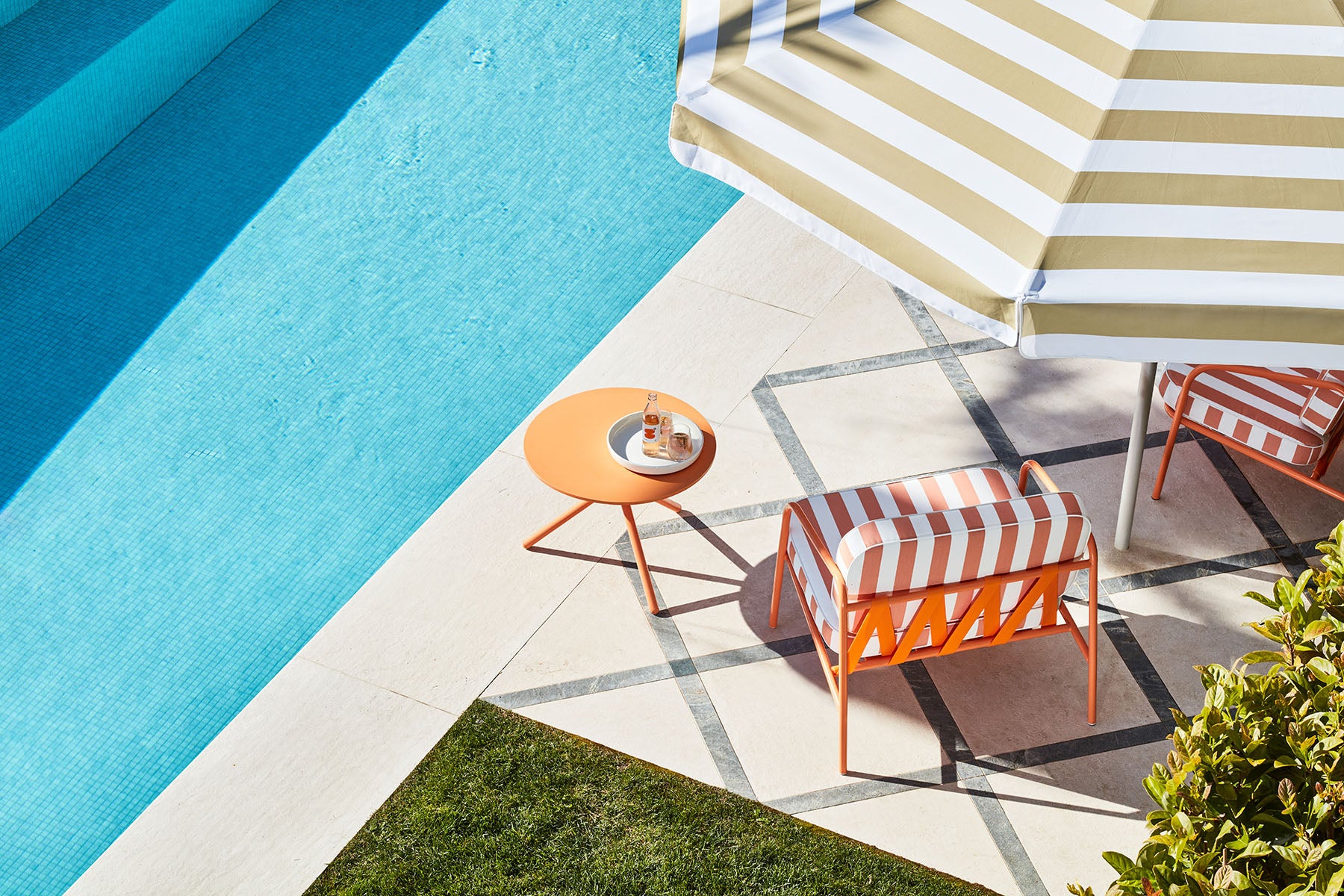 Outdoor Calypso furniture by a pool with striped umbrella and table