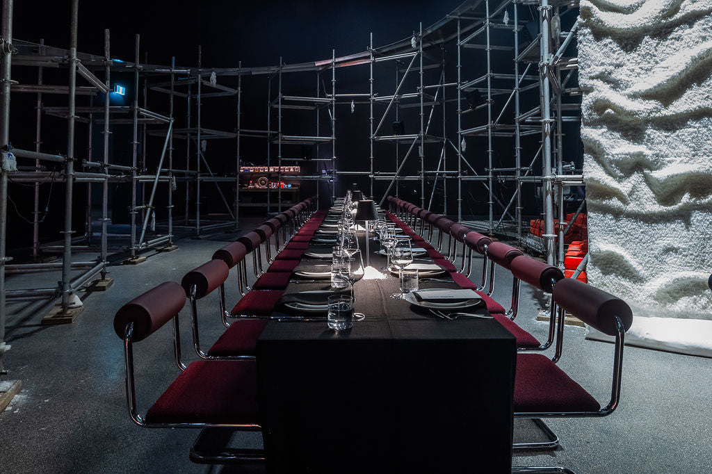 Long dining table set with chairs in a dark room with scaffolding