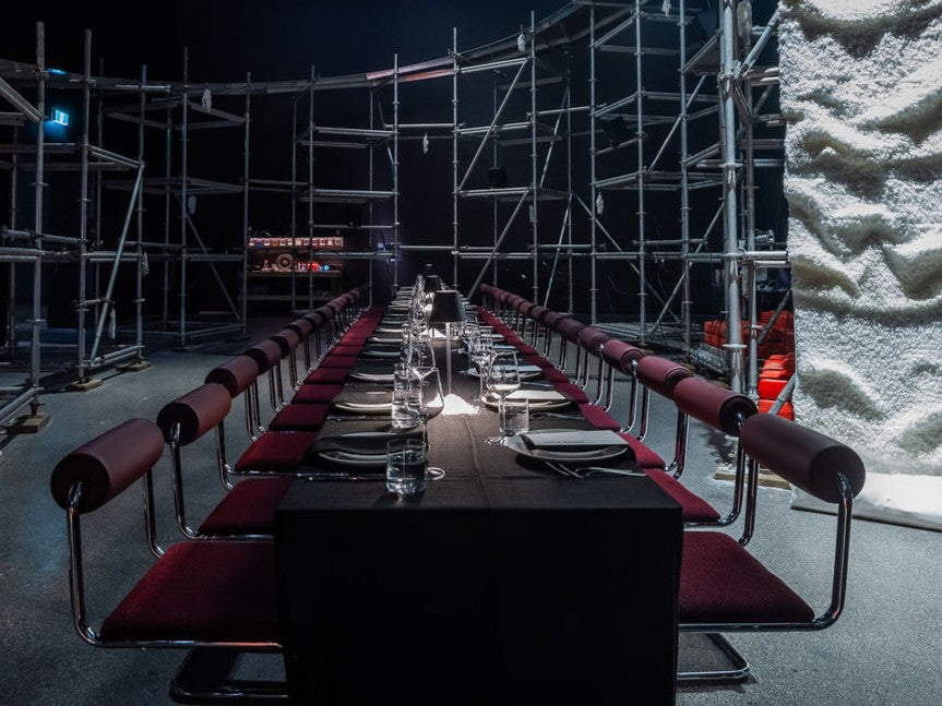 Long dining table set with chairs in a dark room with scaffolding