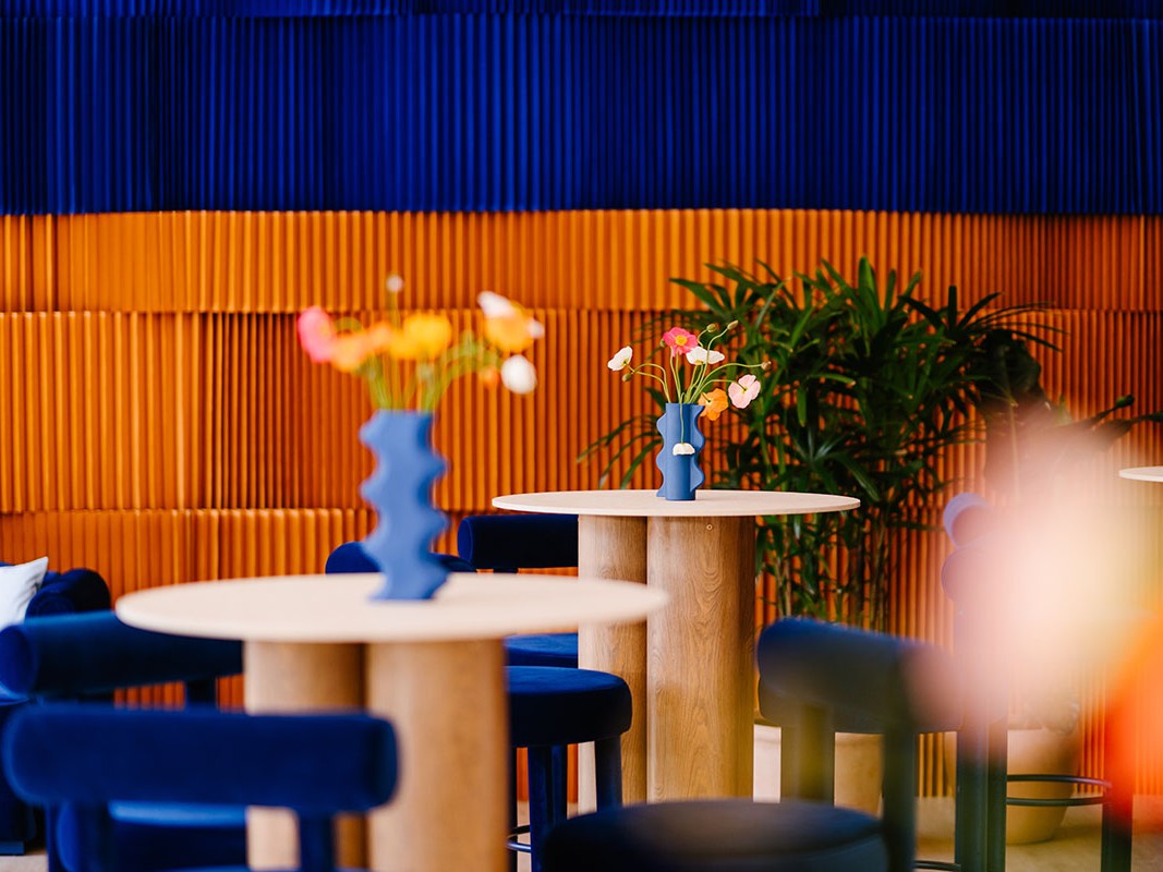 Modern interior with blue chairs, white tables, and decorative vases against a colorful wall. Featuring our Siena Table and Totem Chair
