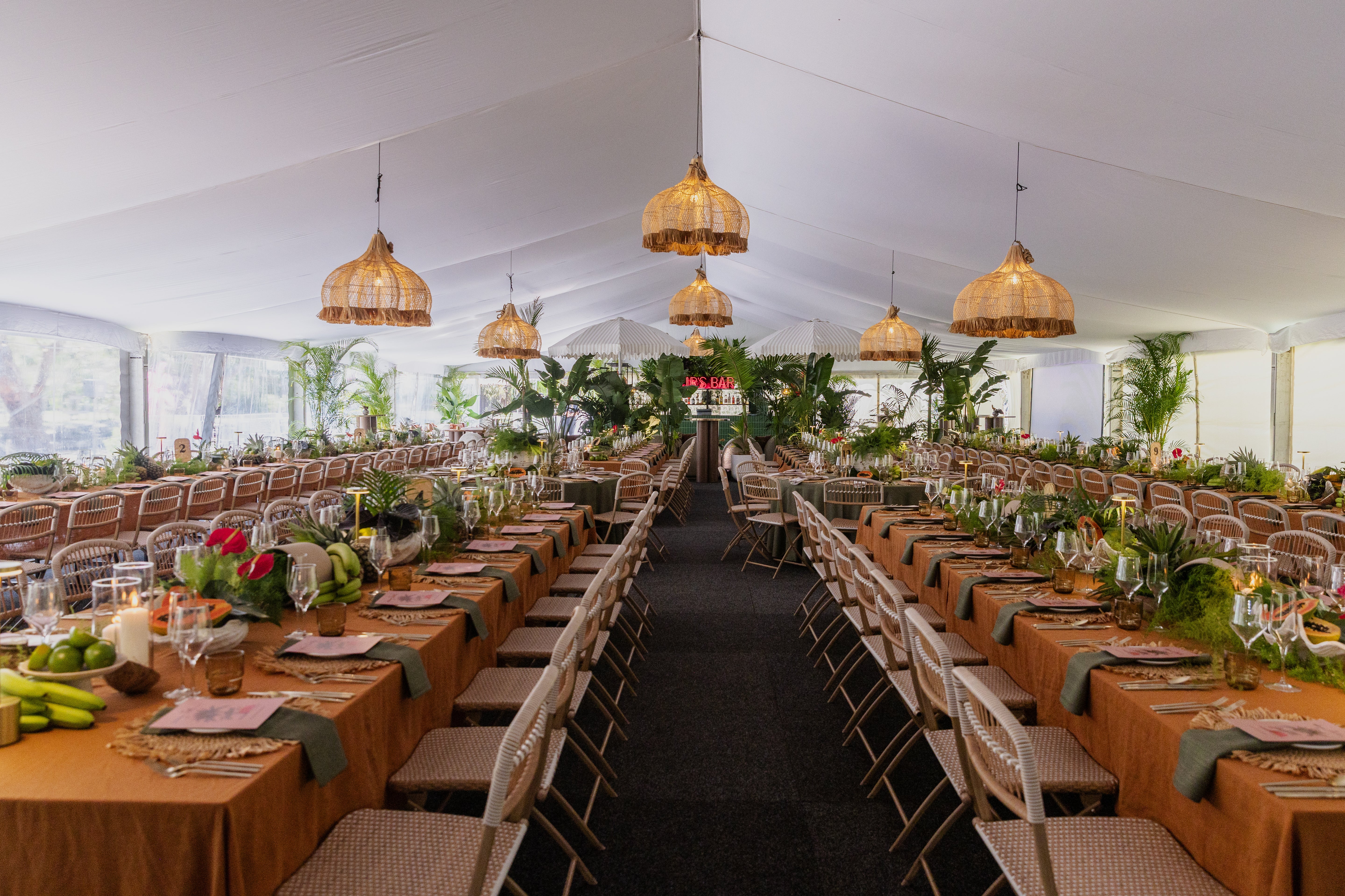 Long table set for a formal event with chairs and decorative elements under a large marquee.