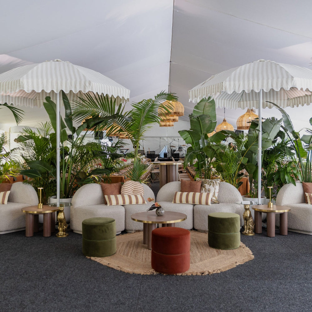 Modern indoor setting with white sofas, decorative pillows, and plants under white umbrellas.